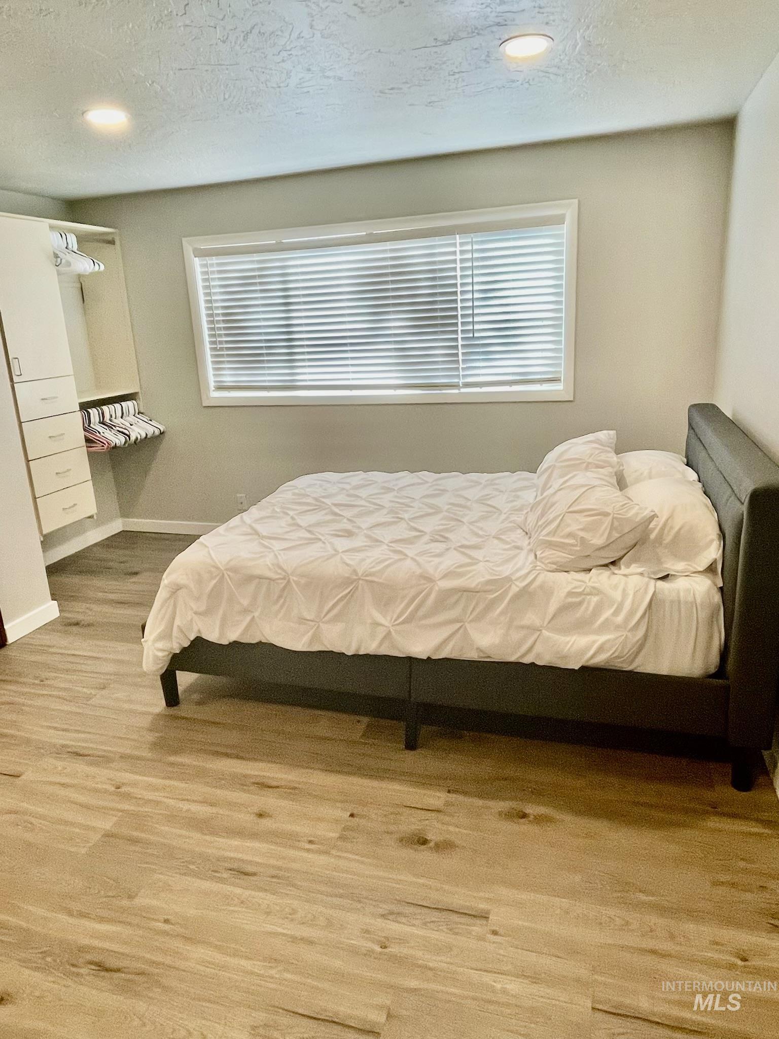 Bedroom with a textured ceiling, multiple windows, light wood-type flooring, and recessed lighting