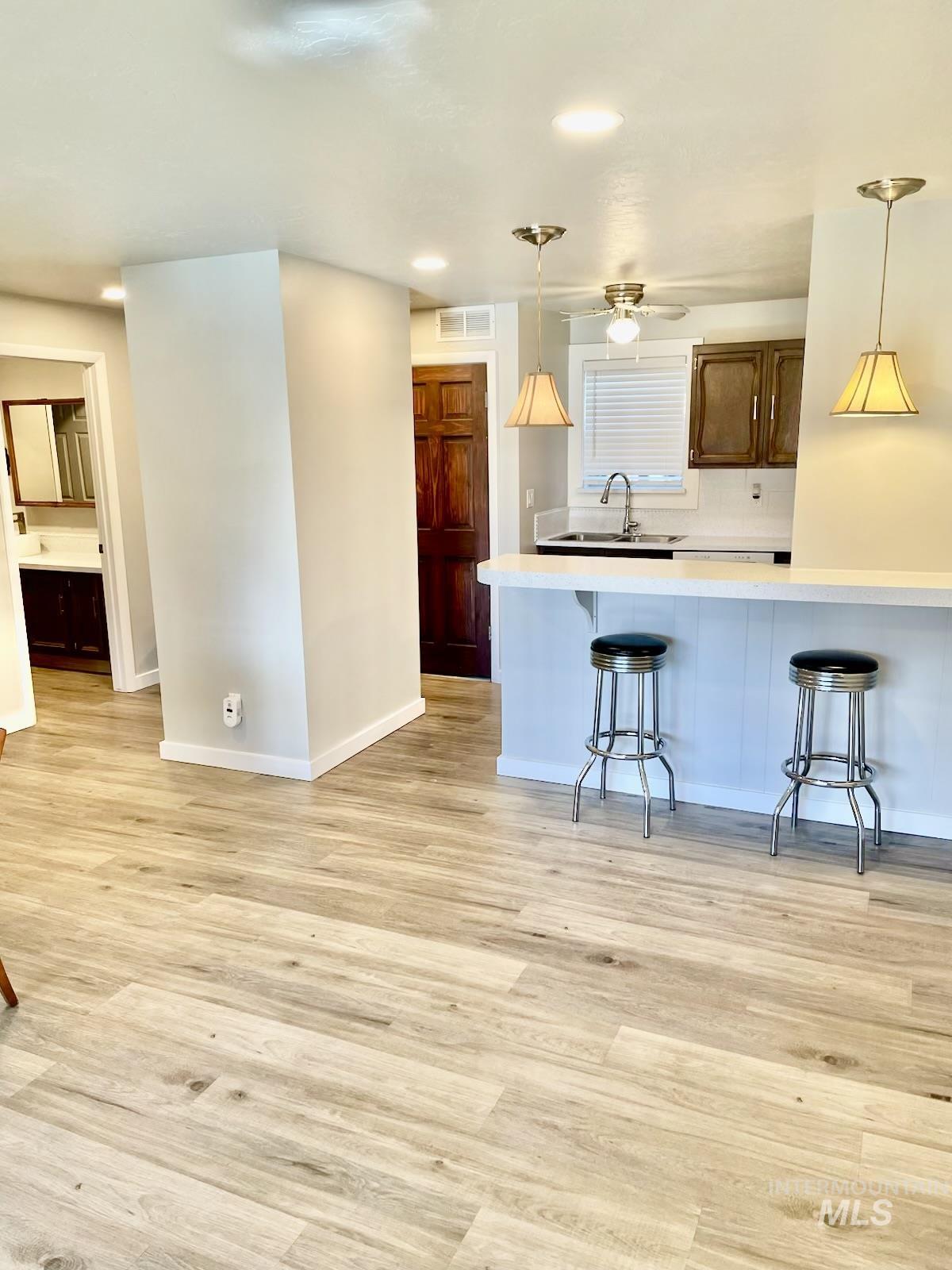 Kitchen with light wood finished floors, light countertops, a breakfast bar, pendant lighting, and recessed lighting