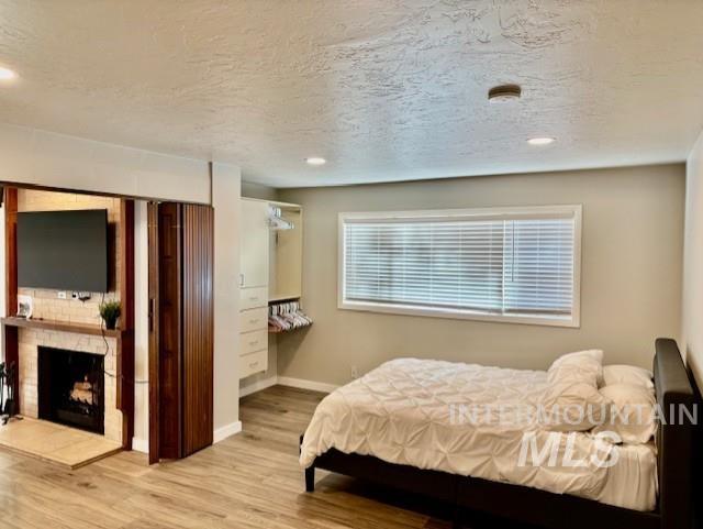 Bedroom featuring wood finished floors, a fireplace with raised hearth, a textured ceiling, and recessed lighting