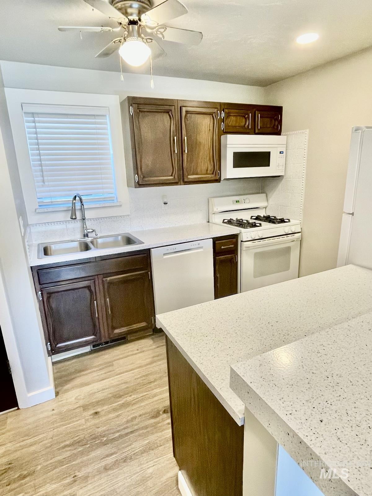 Kitchen featuring white appliances, light wood-style flooring, a ceiling fan, and light stone countertops