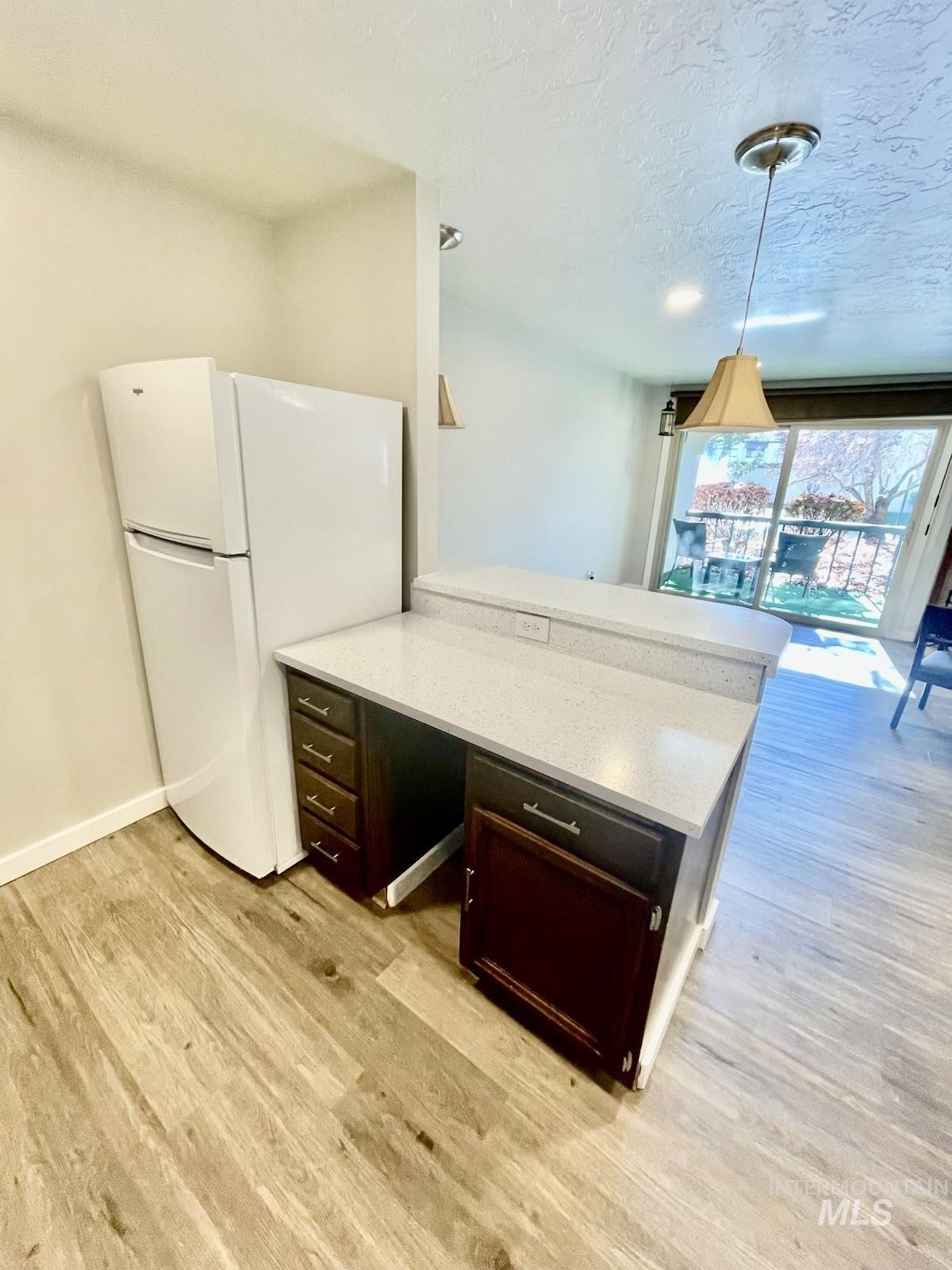 Kitchen featuring freestanding refrigerator, a peninsula, light stone counters, light wood-style flooring, and a textured ceiling
