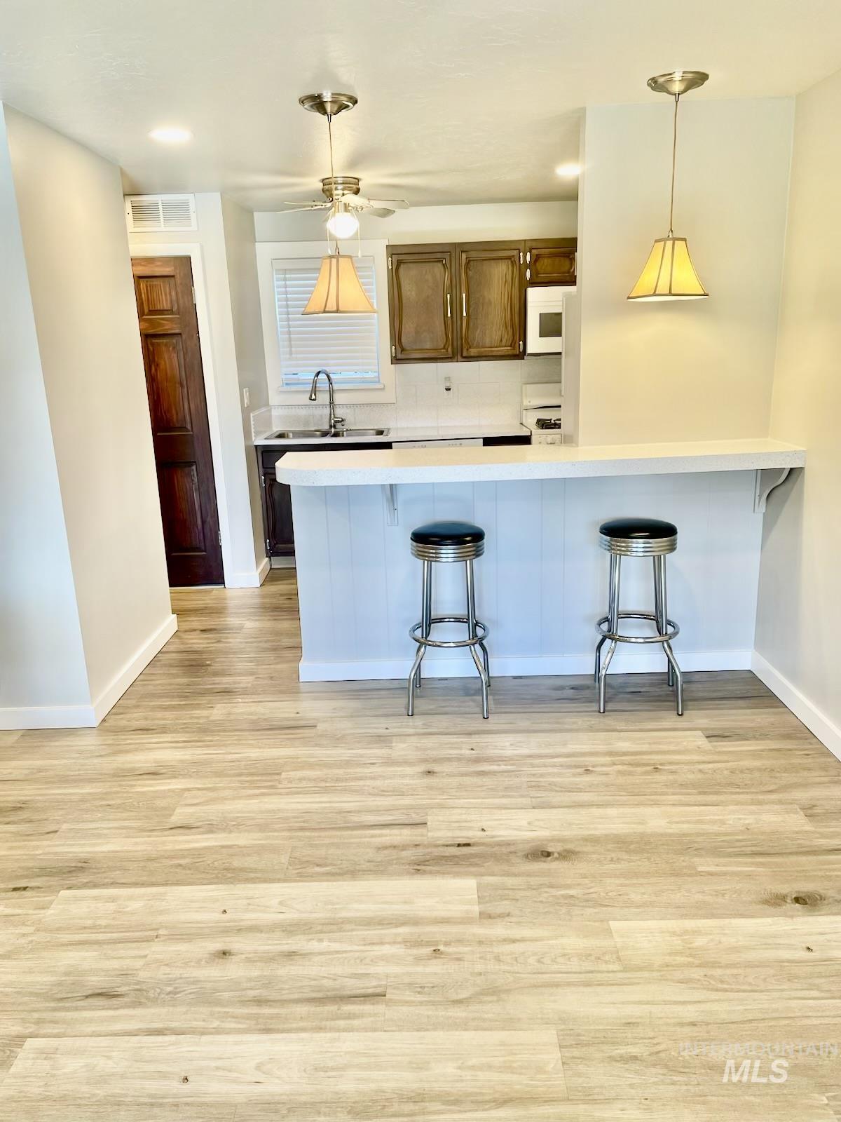 Kitchen with a peninsula, a kitchen breakfast bar, pendant lighting, and light wood finished floors