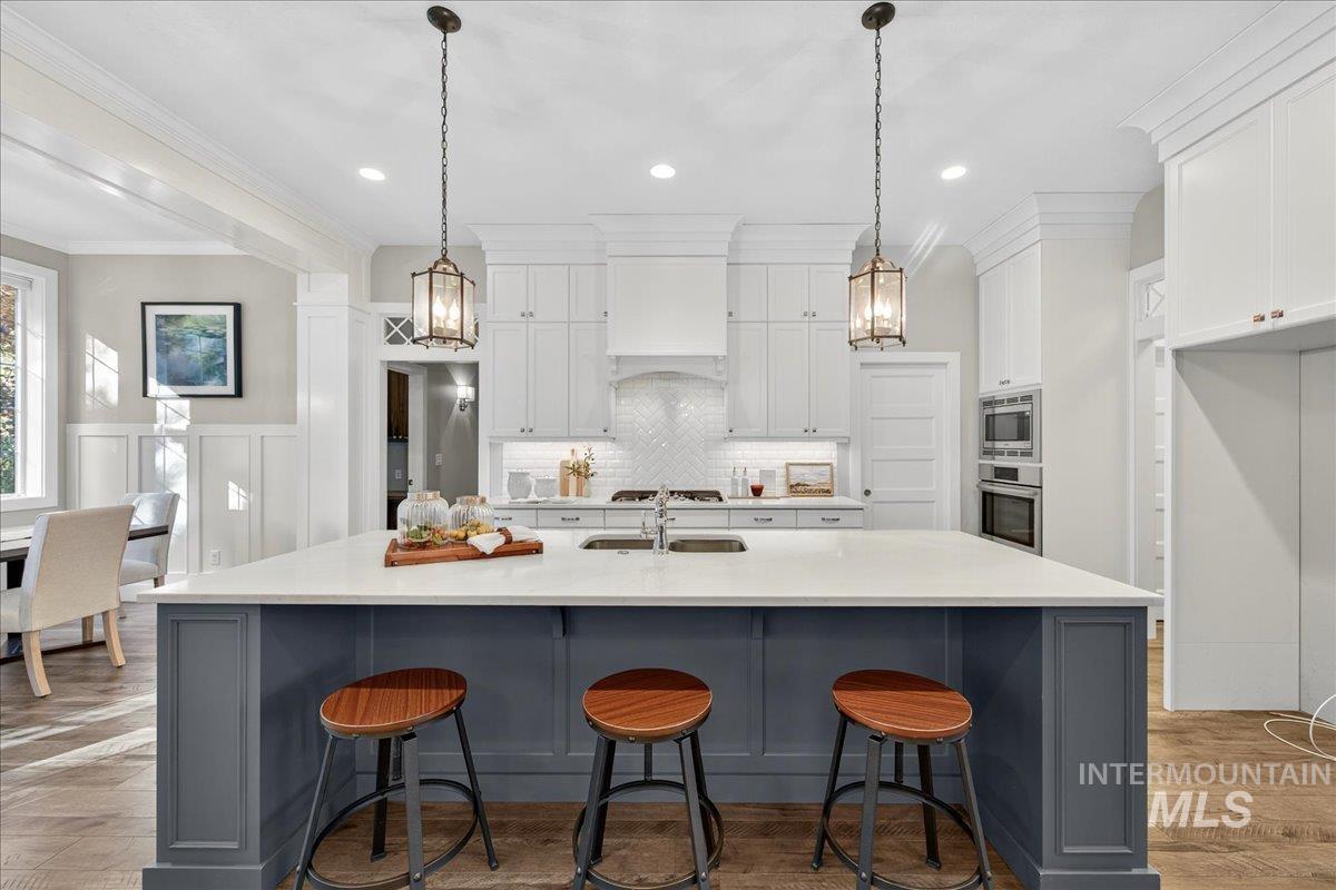 Kitchen with gray cabinetry, white cabinets, crown molding, light wood-style floors, and a kitchen breakfast bar