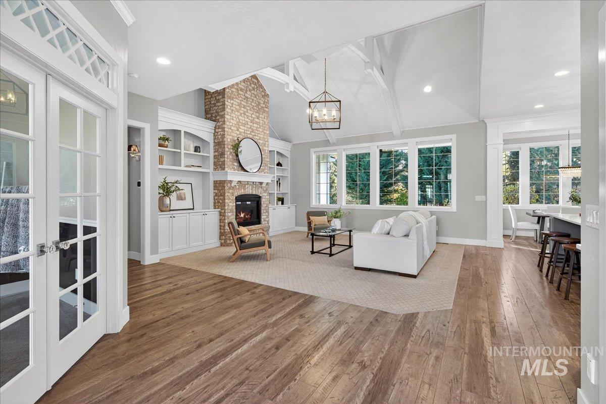 Living room with hardwood / wood-style flooring, a brick fireplace, a chandelier, built in shelves, and ornamental molding