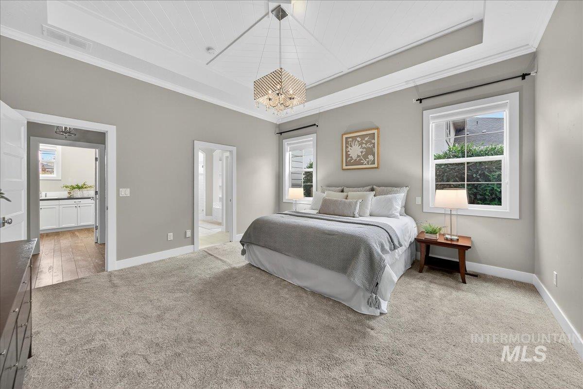 Bedroom featuring ornamental molding, a tray ceiling, a chandelier, and light colored carpet