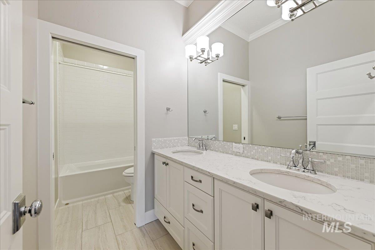 Bathroom with double vanity, ornamental molding, and shower / bath combination