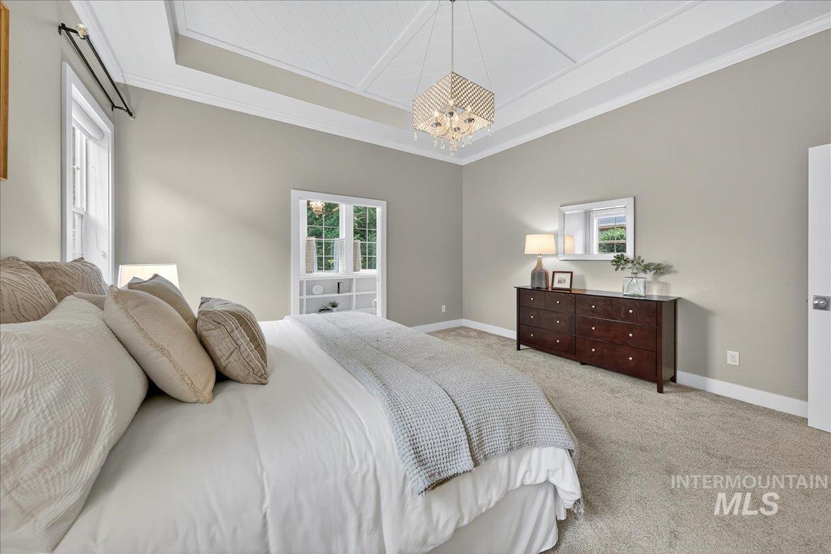 Bedroom with carpet, ornamental molding, a raised ceiling, and a chandelier