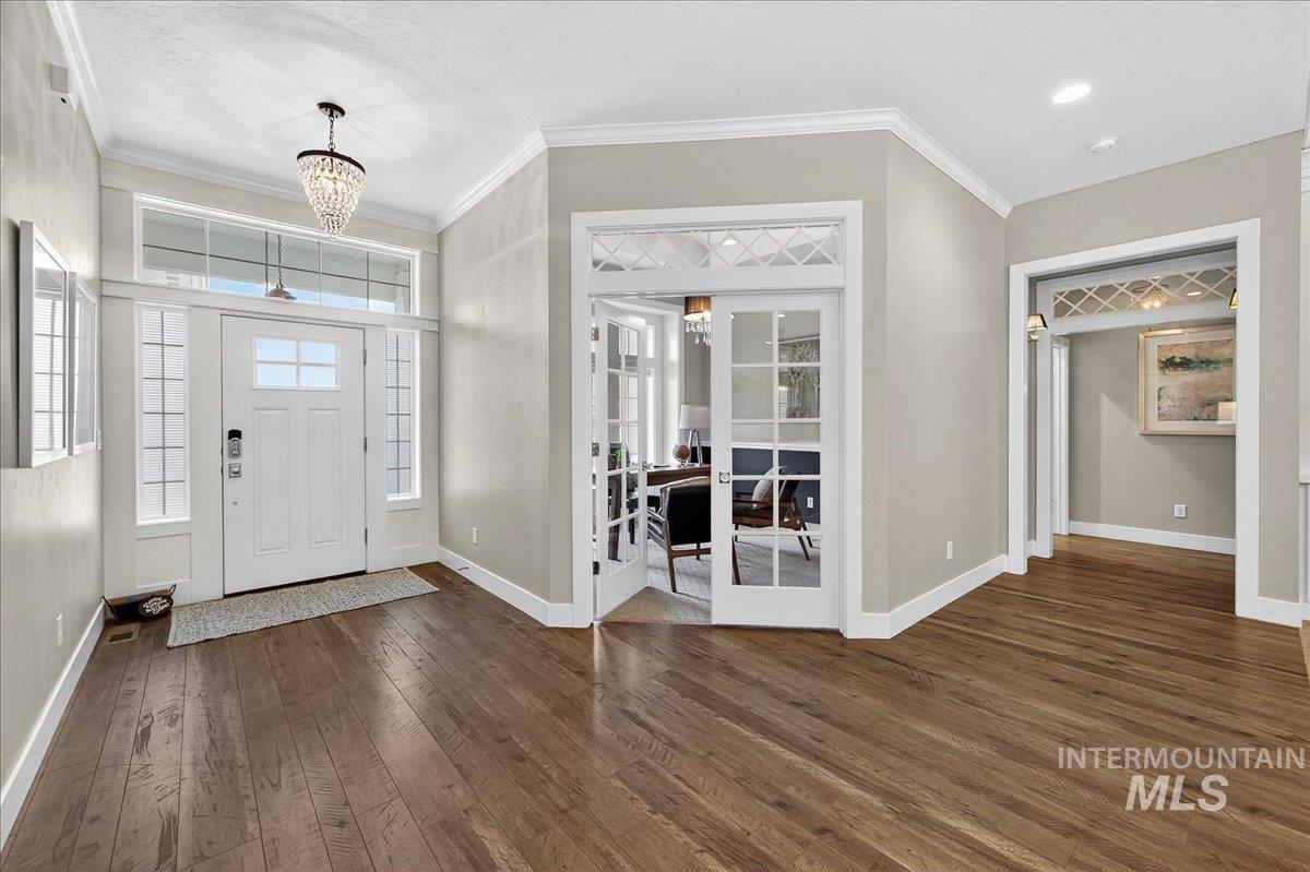Entrance foyer featuring french doors, a chandelier, dark wood-type flooring, and ornamental molding