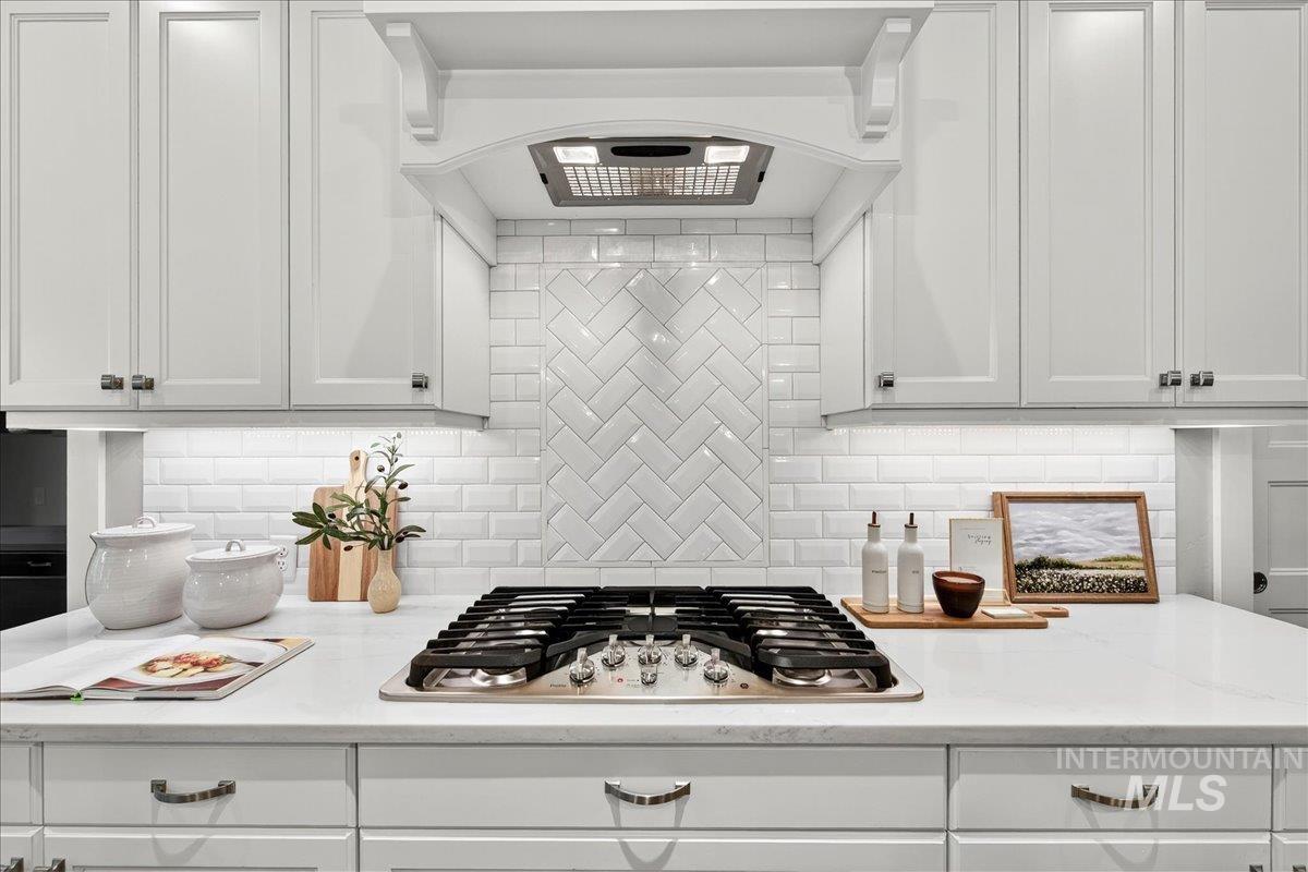 Kitchen with wall chimney range hood, white cabinets, stainless steel gas stovetop, decorative backsplash, and light stone countertops