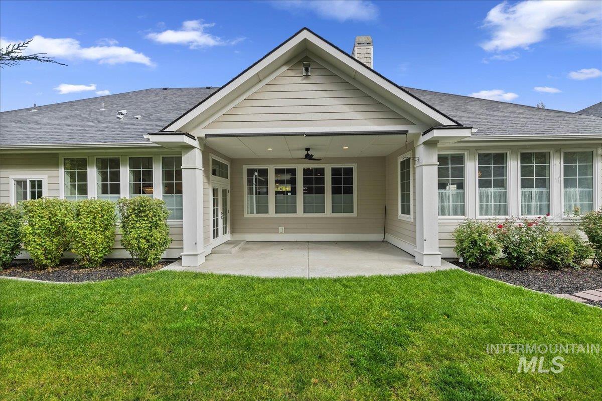 Rear view of house with ceiling fan, a patio area, roof with shingles, and a lawn