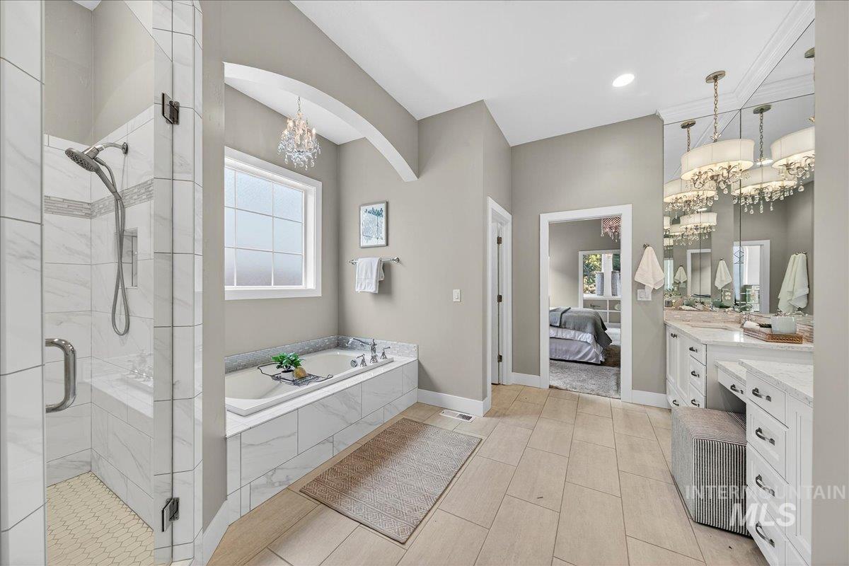 Bathroom with vanity, a chandelier, a shower stall, a garden tub, and healthy amount of natural light