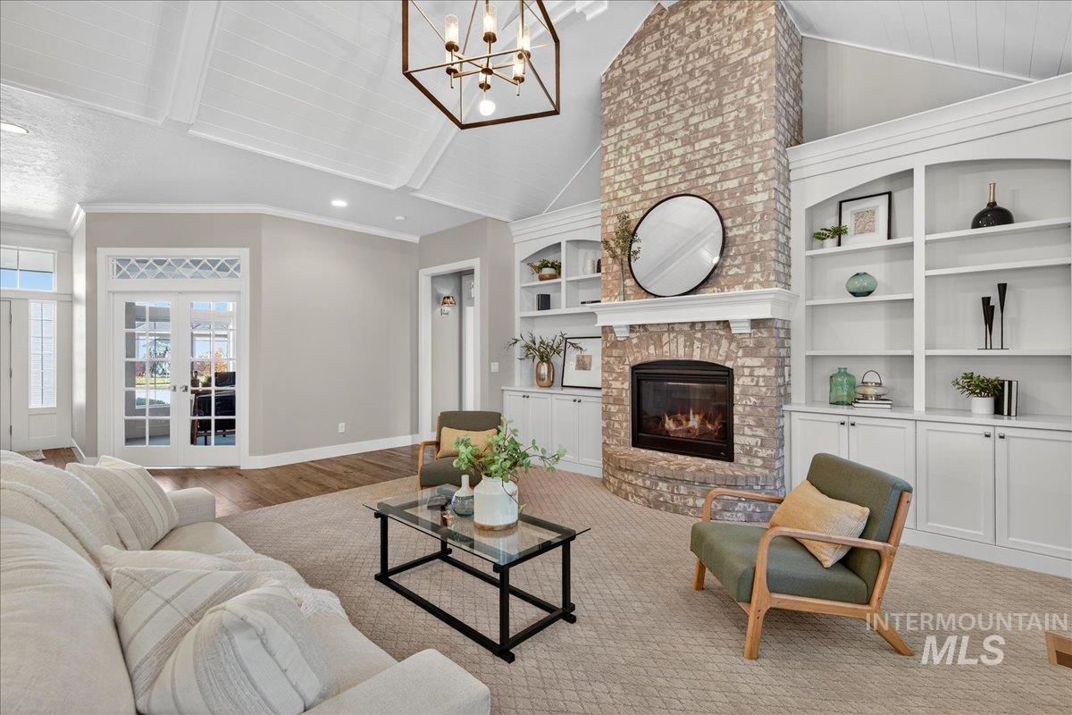 Living room featuring vaulted ceiling, french doors, crown molding, a brick fireplace, and a chandelier