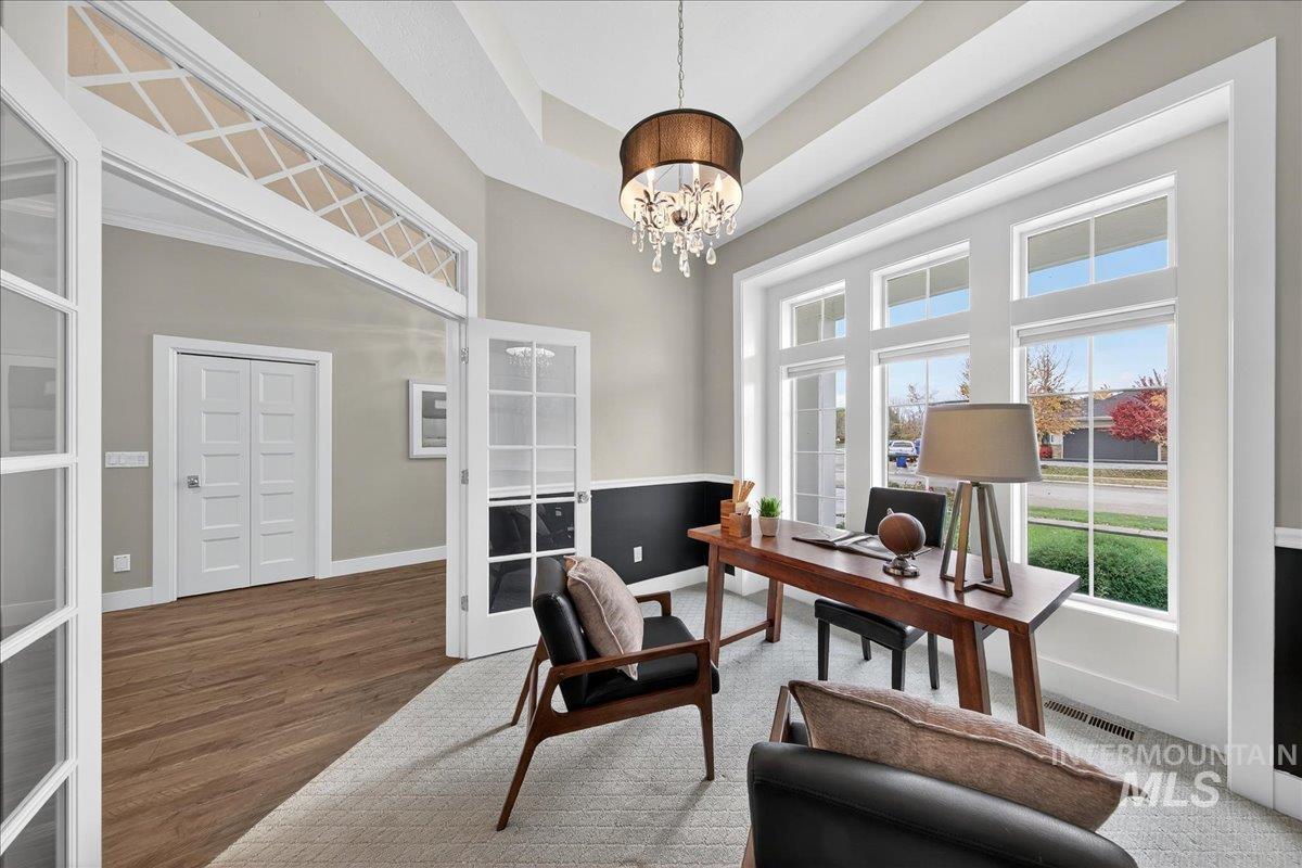 Office with french doors, a towering ceiling, a chandelier, a tray ceiling, and wood finished floors
