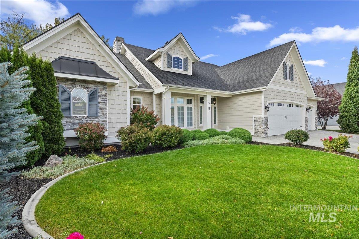 View of front of property with a shingled roof, stone siding, a front lawn, and concrete driveway