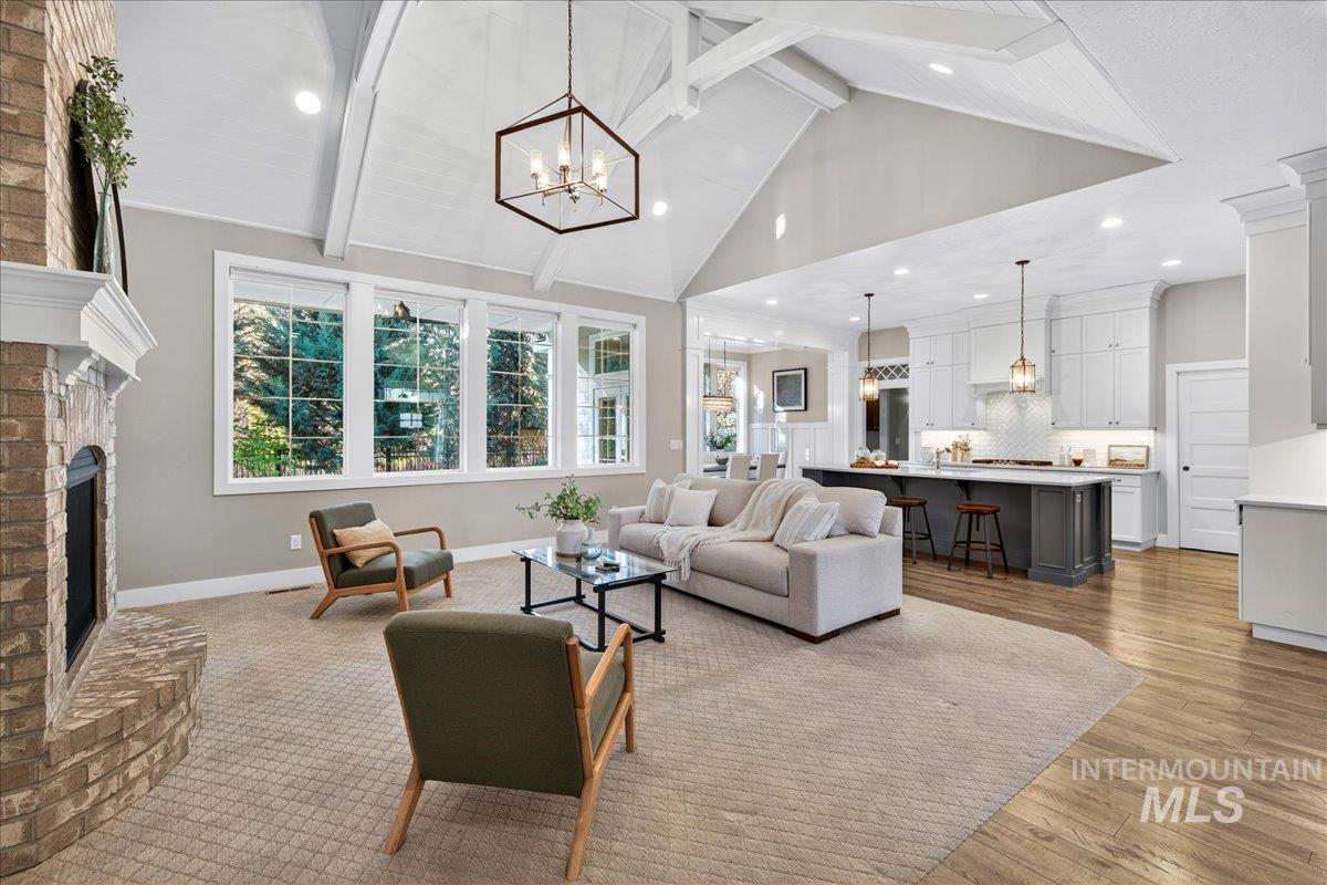 Living room featuring a chandelier, beam ceiling, a brick fireplace, high vaulted ceiling, and light wood-type flooring