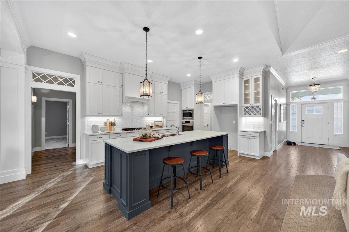 Kitchen with a breakfast bar, white cabinetry, backsplash, an island with sink, and crown molding