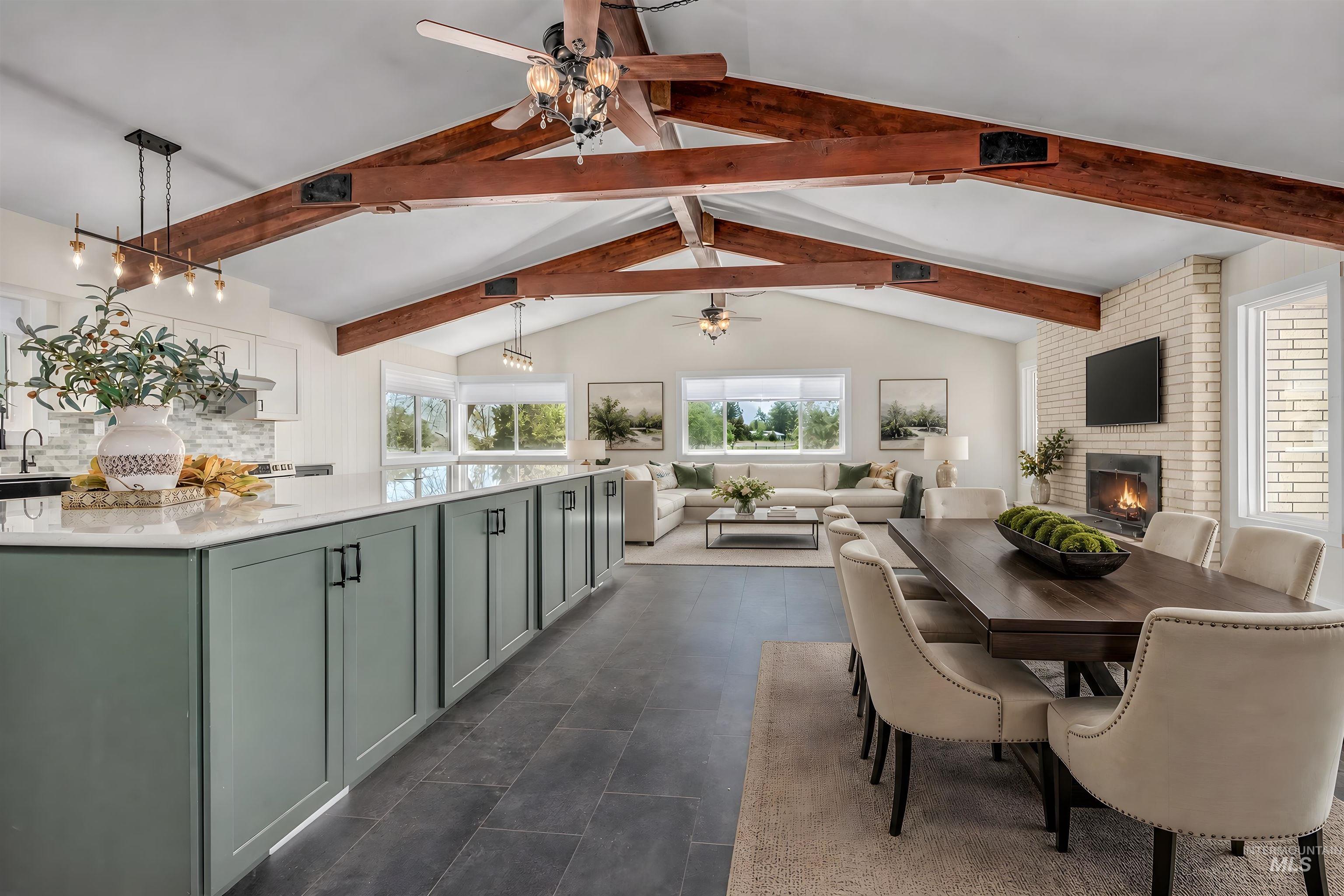 Open-concept living space featuring vaulted ceilings with exposed wood beams, a light brick fireplace, and a kitchen island with stone countertops and green cabinetry