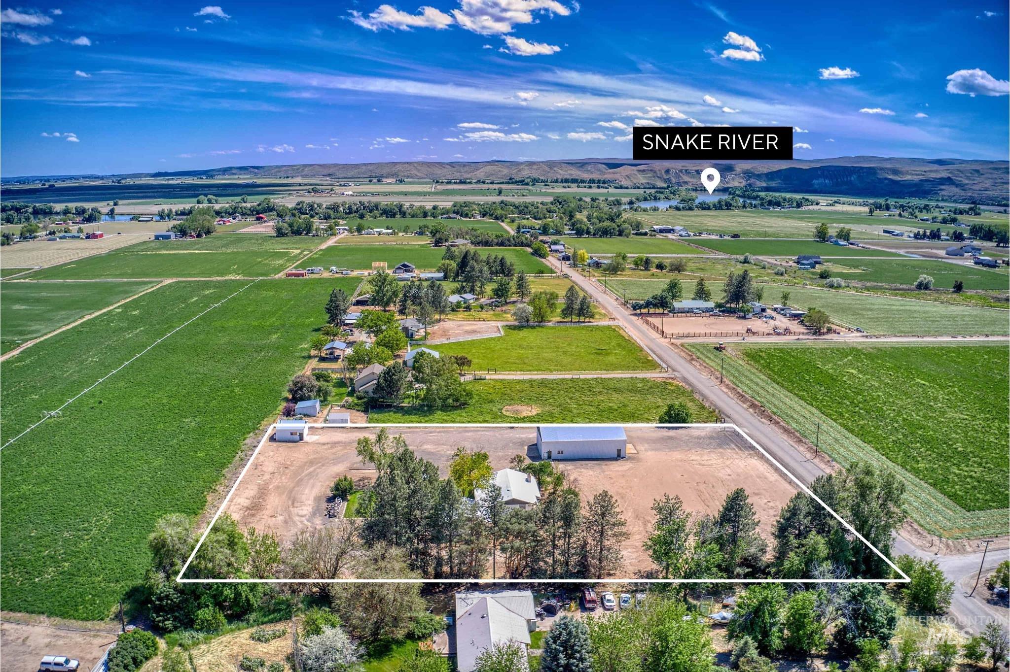 Expansive rural property featuring a large white outbuilding, mature trees, and a gravel driveway