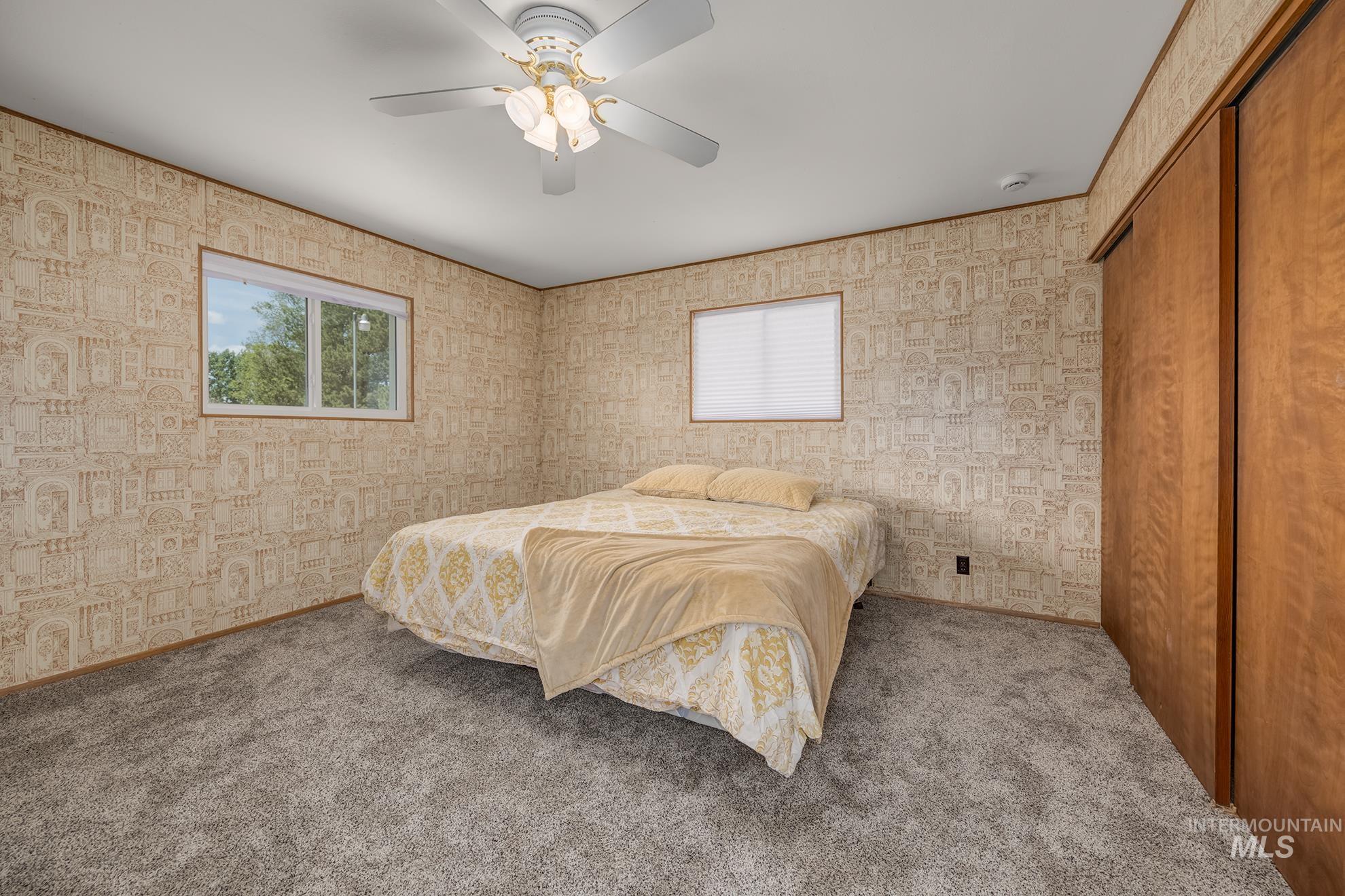 Bedroom featuring patterned wallpaper, carpeted flooring, and two windows