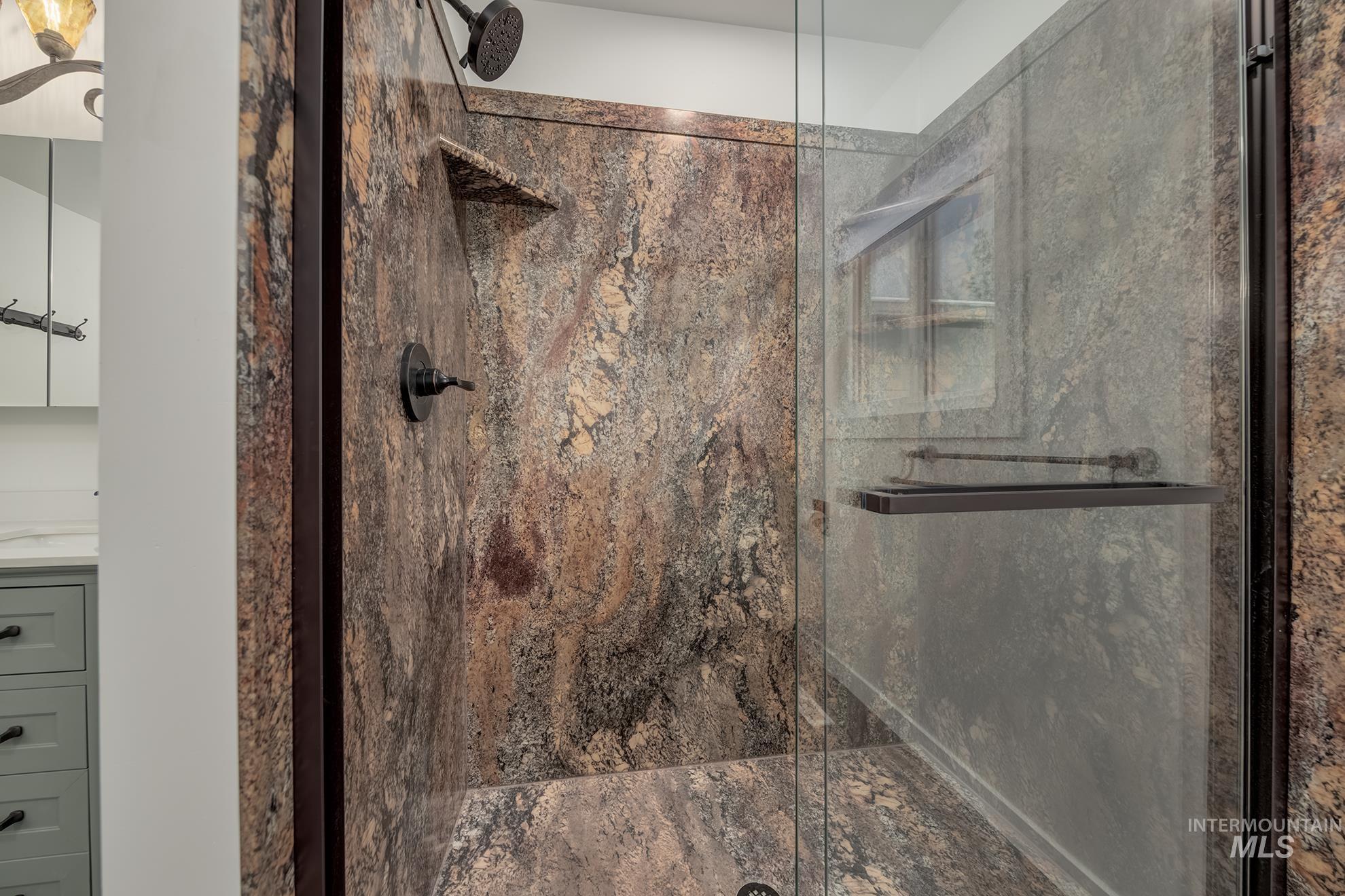 Walk-in shower with natural stone-finish walls, a built-in shelf, and a dark bronze shower fixture