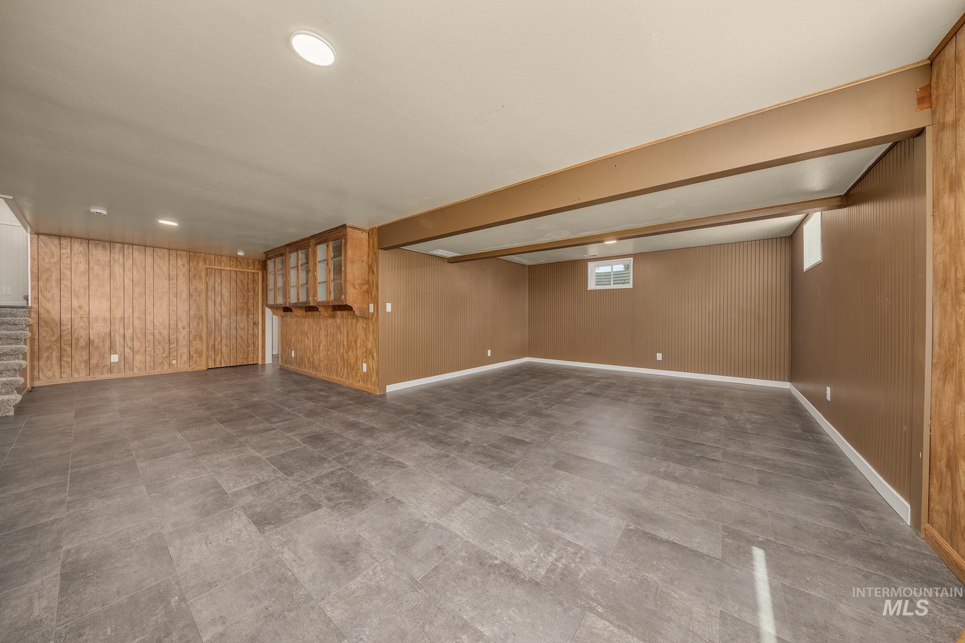 Spacious lower-level room featuring wood-finish wall paneling, ceiling-mounted lighting, and durable tile flooring