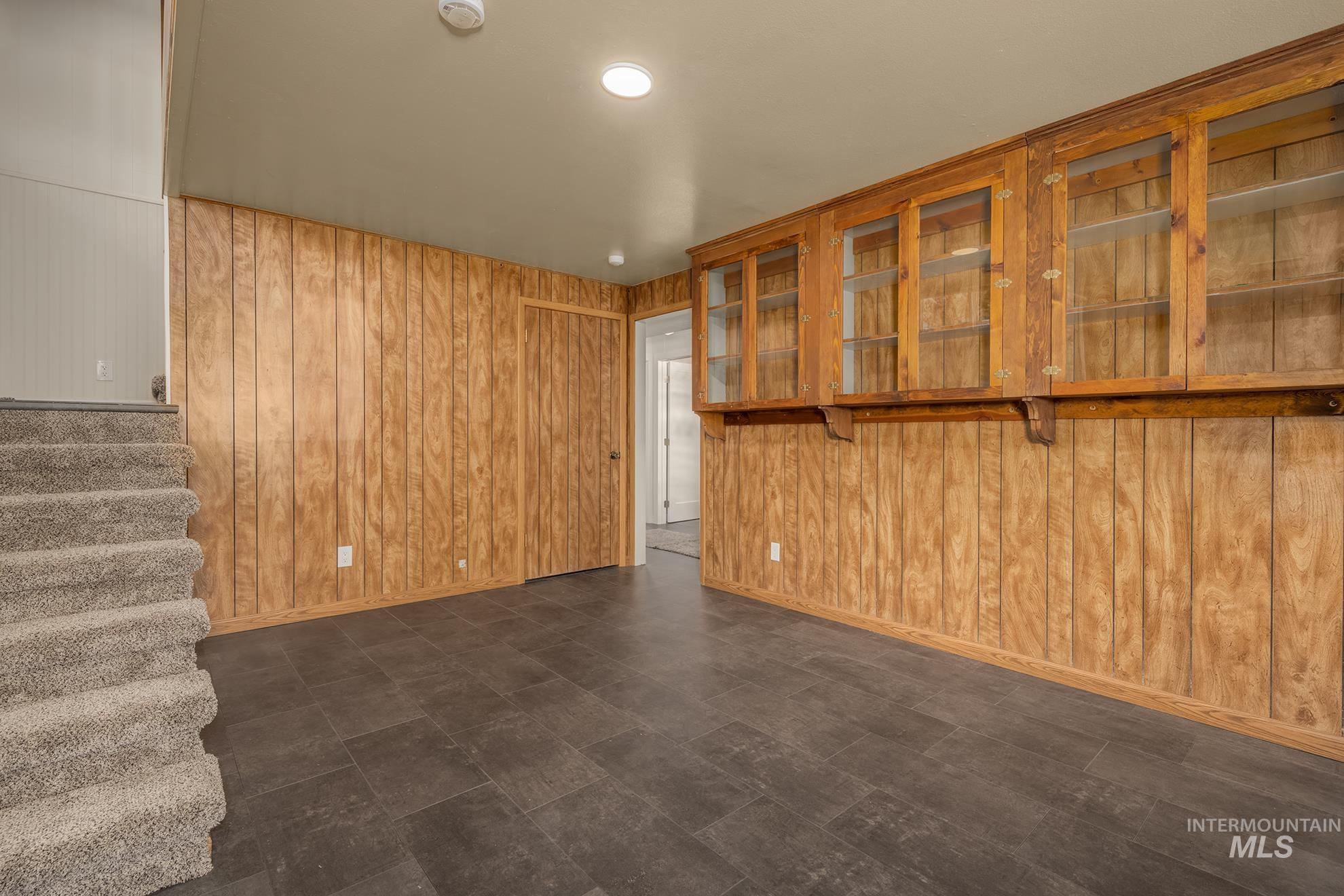 Recessed lighting illuminating a finished space featuring wood paneling, built-in display cabinetry with glass doors, and dark tile flooring