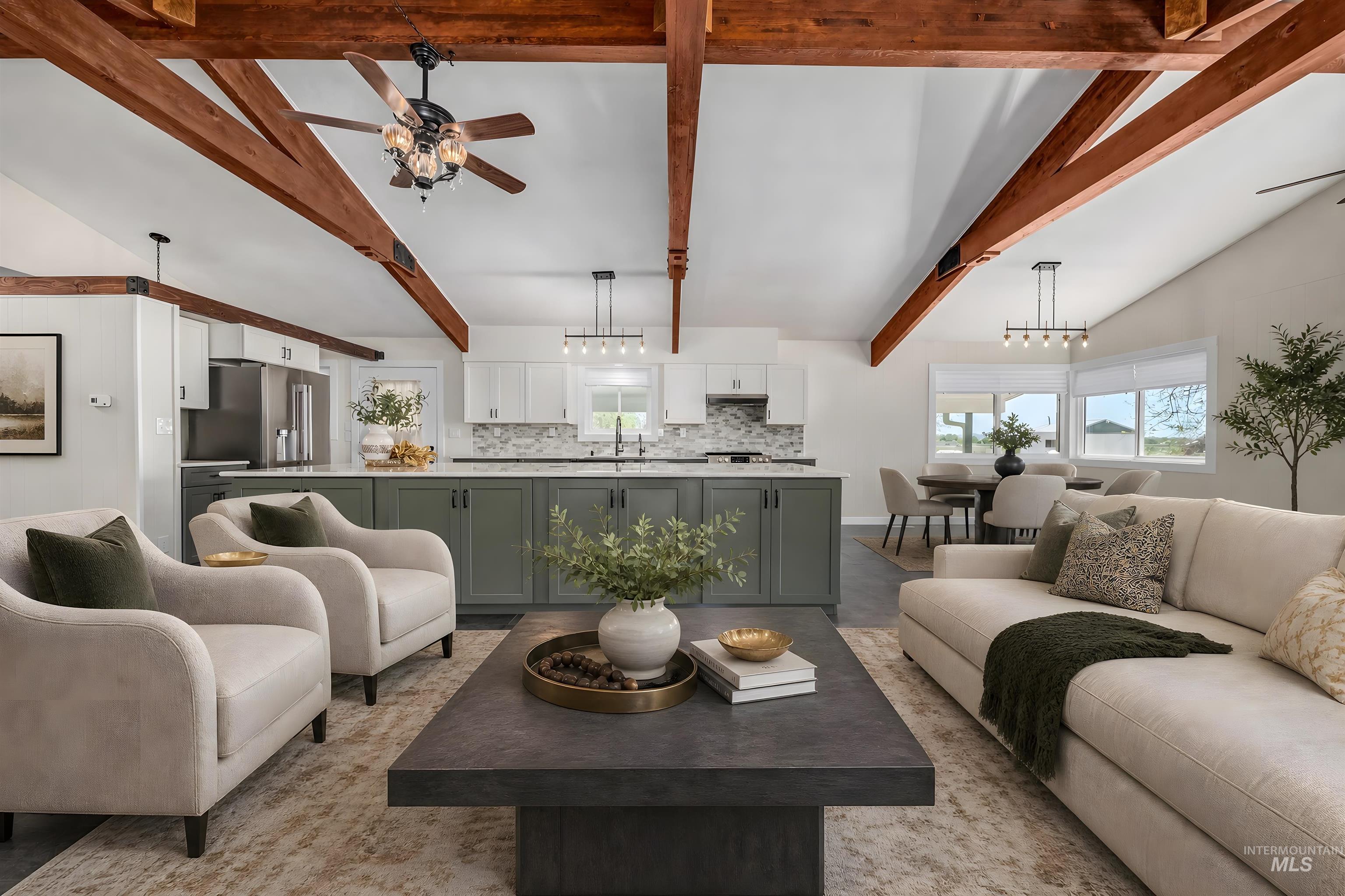 Open-concept living space featuring vaulted ceilings with exposed wood beams, a contemporary kitchen island with a light-toned countertop, stainless steel appliances, and a dining area with multiple windows