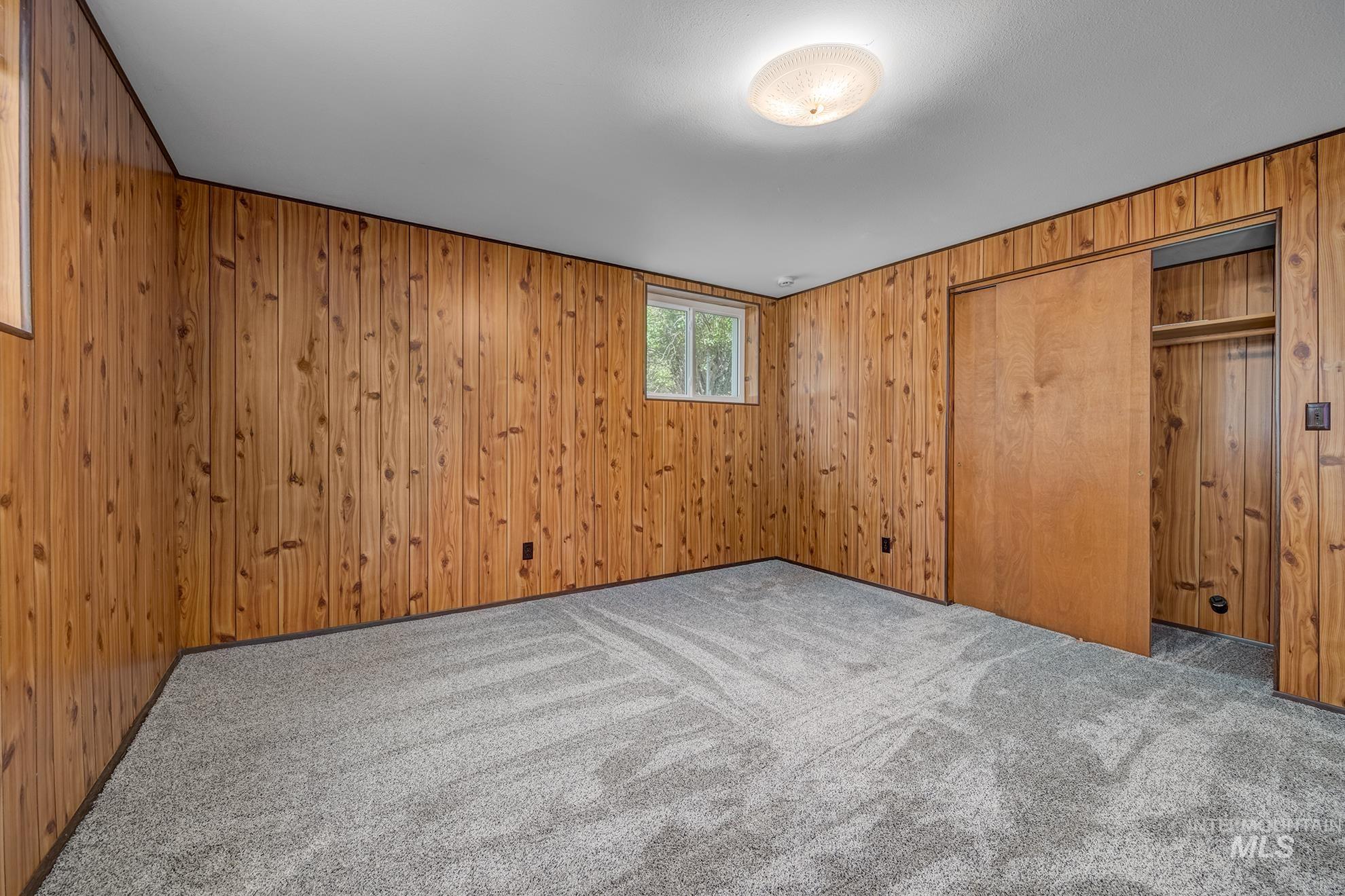 Interior room featuring wood paneling, light gray carpeting, and a window providing natural illumination