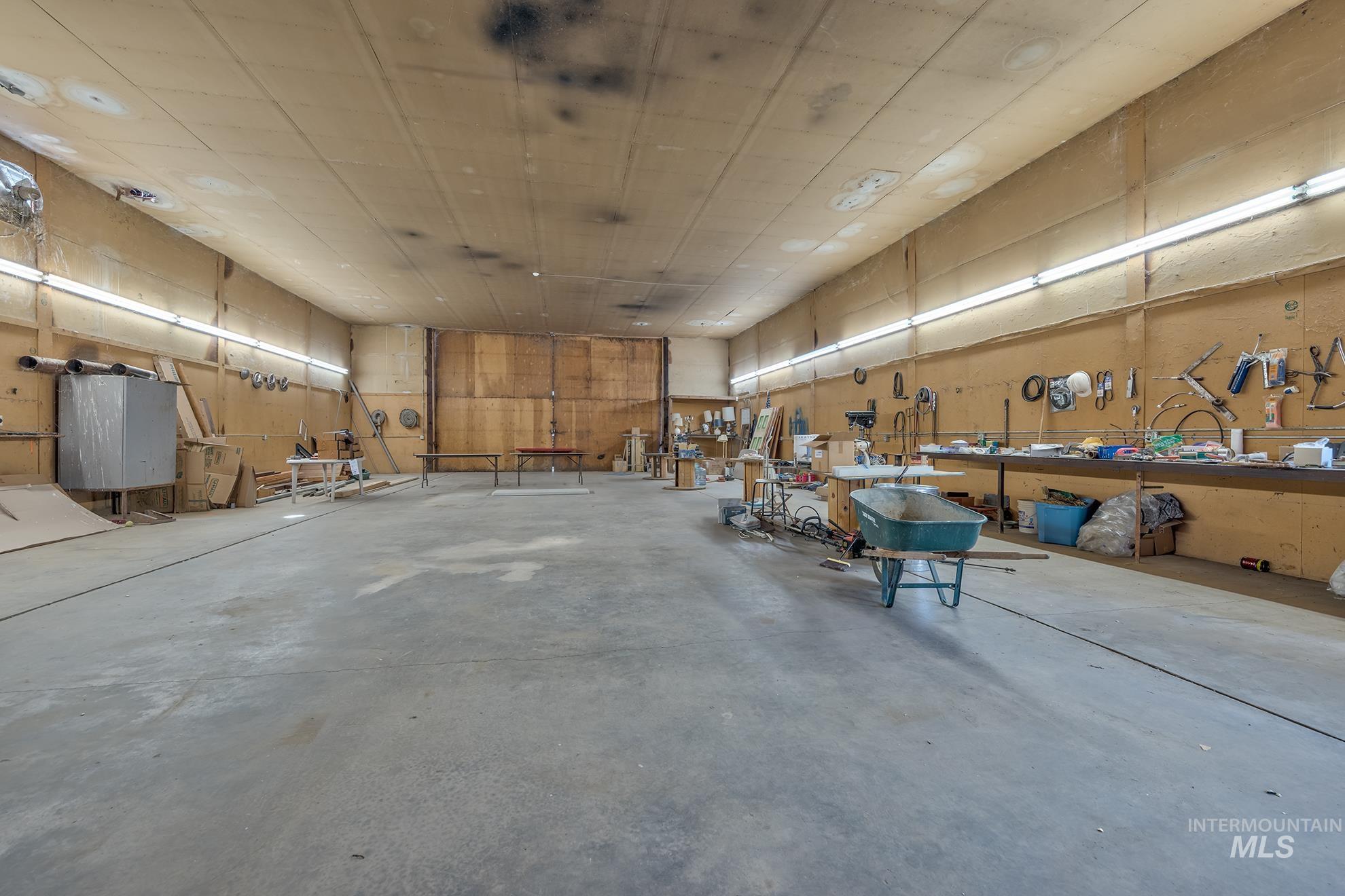 Expansive workshop featuring a concrete floor, plywood walls, and overhead fluorescent lighting