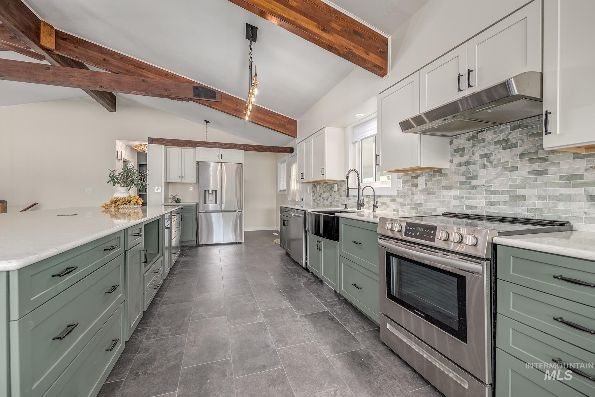 Modern kitchen featuring vaulted ceilings with exposed wood beams, stainless steel appliances, a large center island with a light-toned countertop, and a mosaic tile backsplash