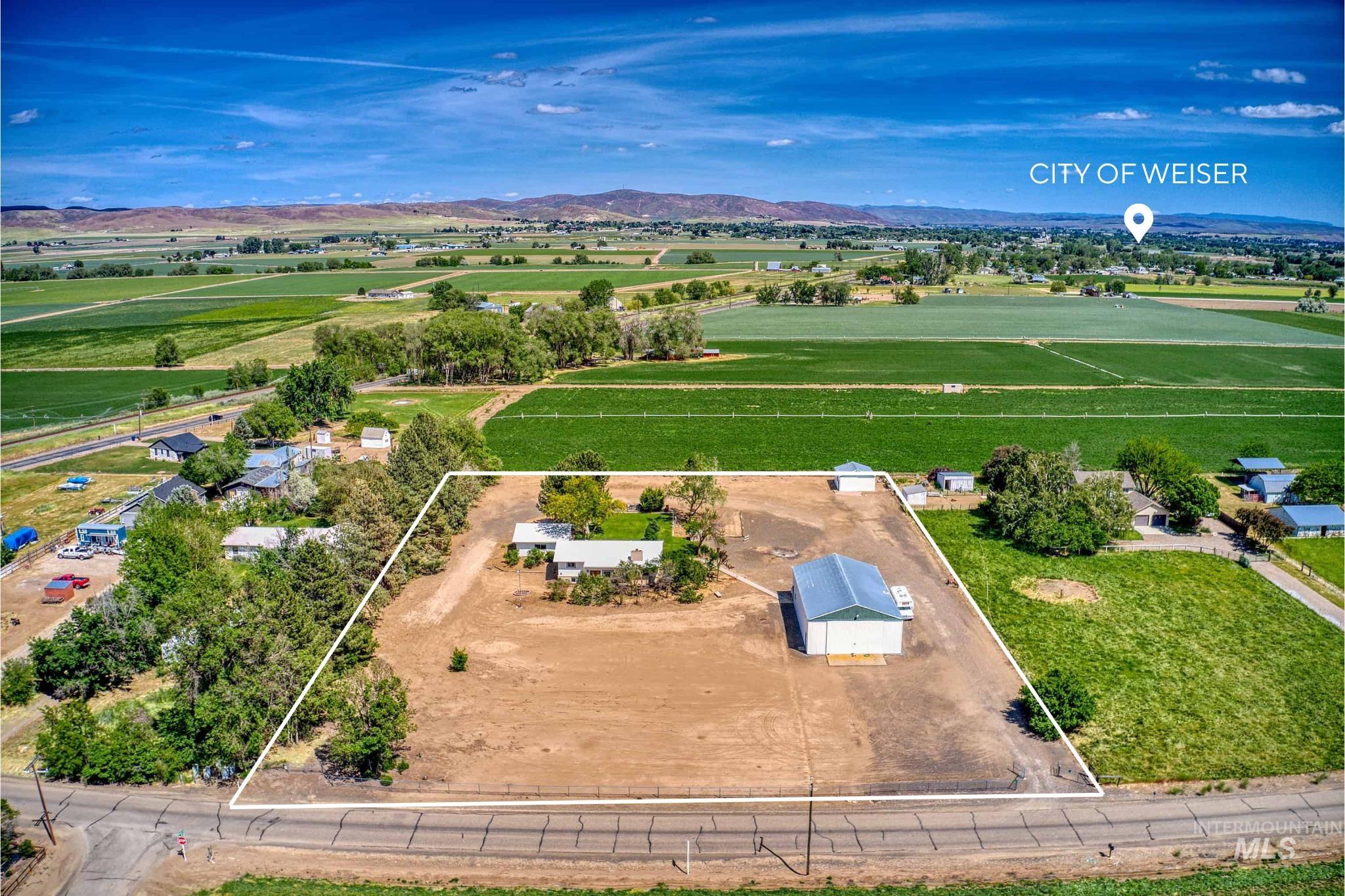 Expansive agricultural property featuring a primary residence with a light-colored roof, a large metal-sided outbuilding, and significant undeveloped land