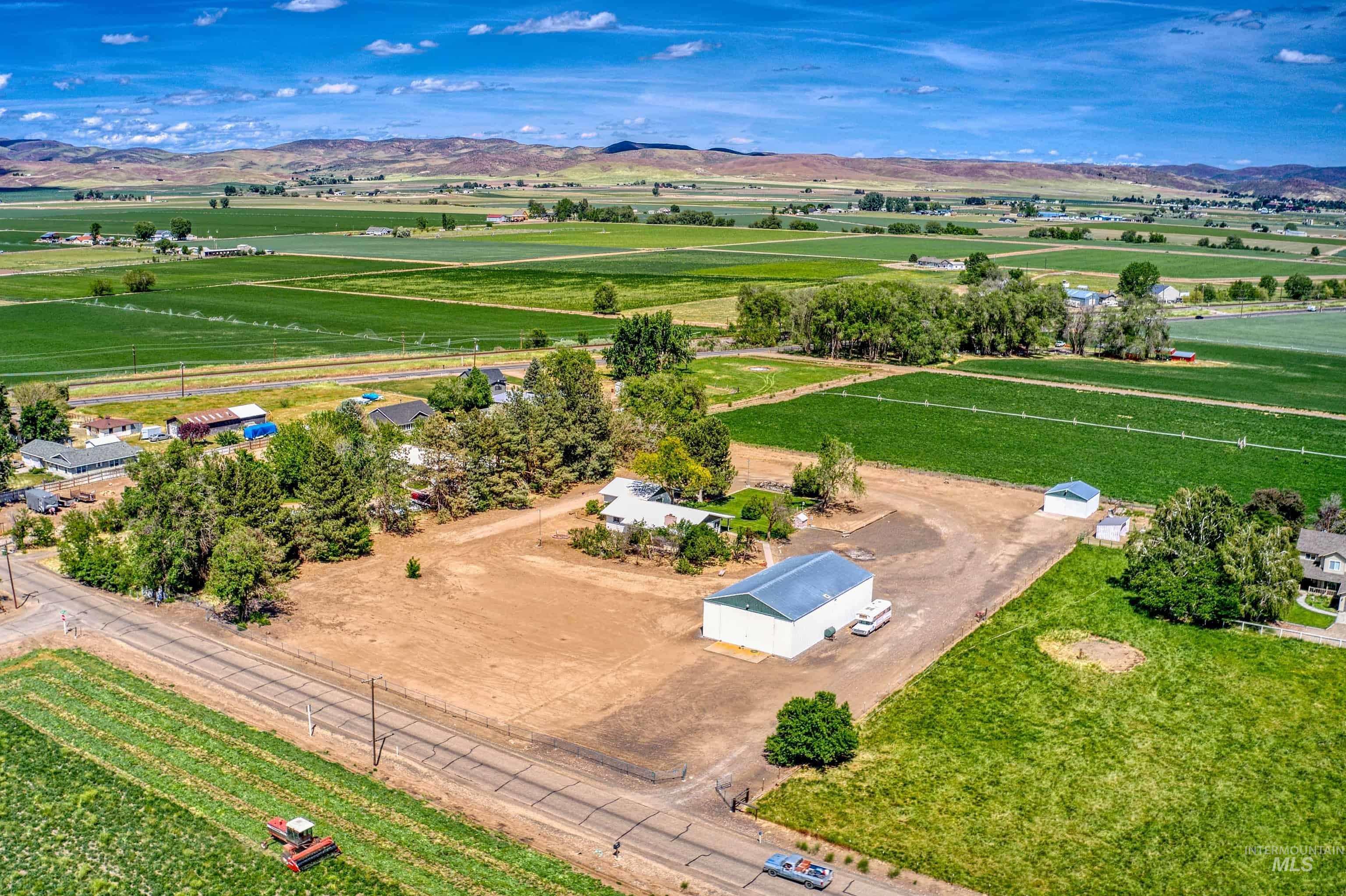 Expansive rural property featuring a large metal building with a blue roof, mature trees, and a spacious lot