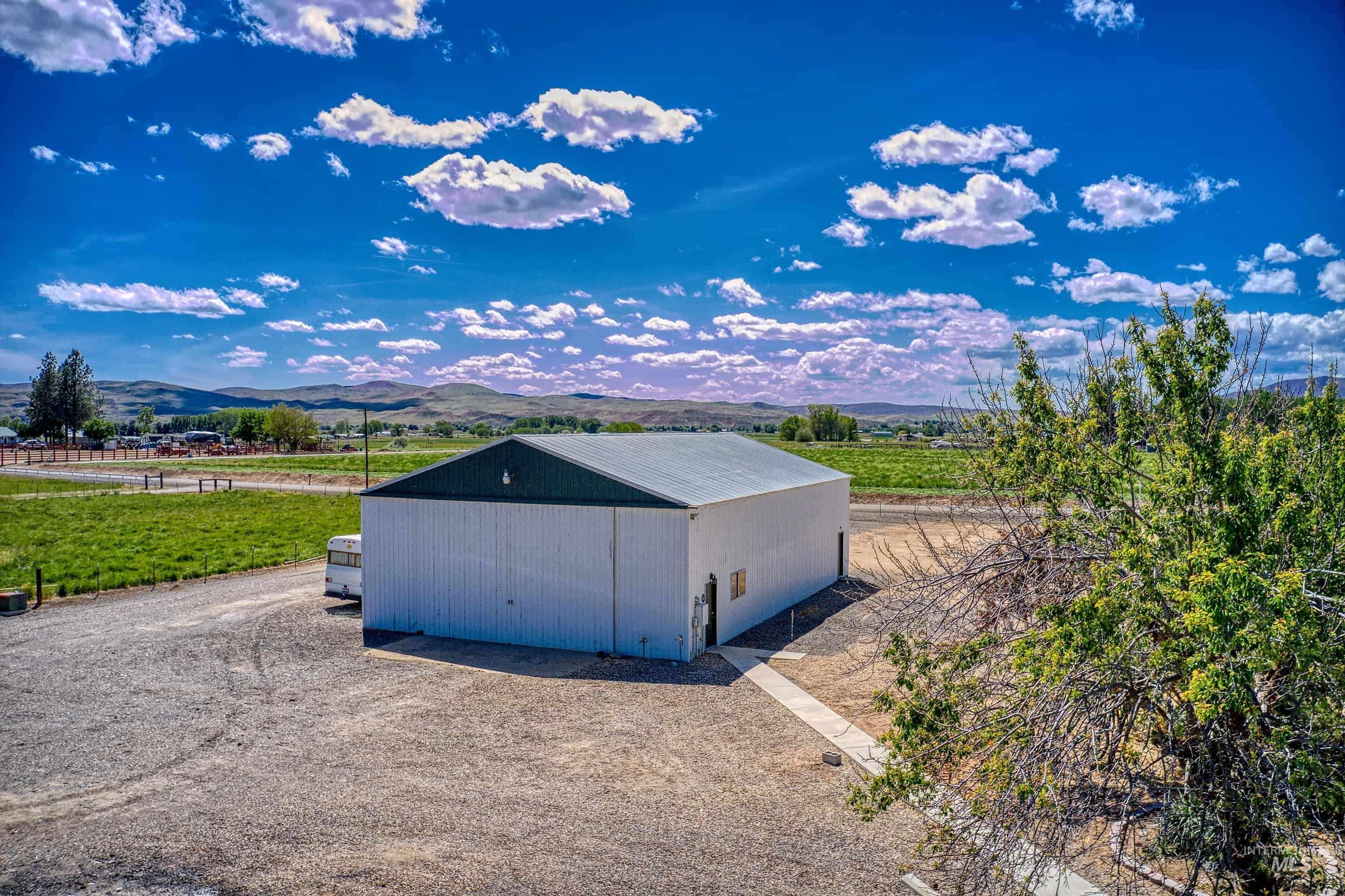 Spacious agricultural building with a white metal exterior and dark green roof, situated on a large gravel lot