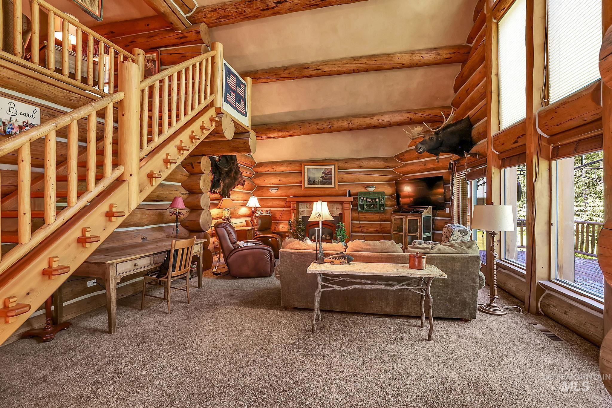 Spacious interior featuring exposed log construction, a log staircase with balusters, high ceilings, large windows, and a built-in desk under the stairs