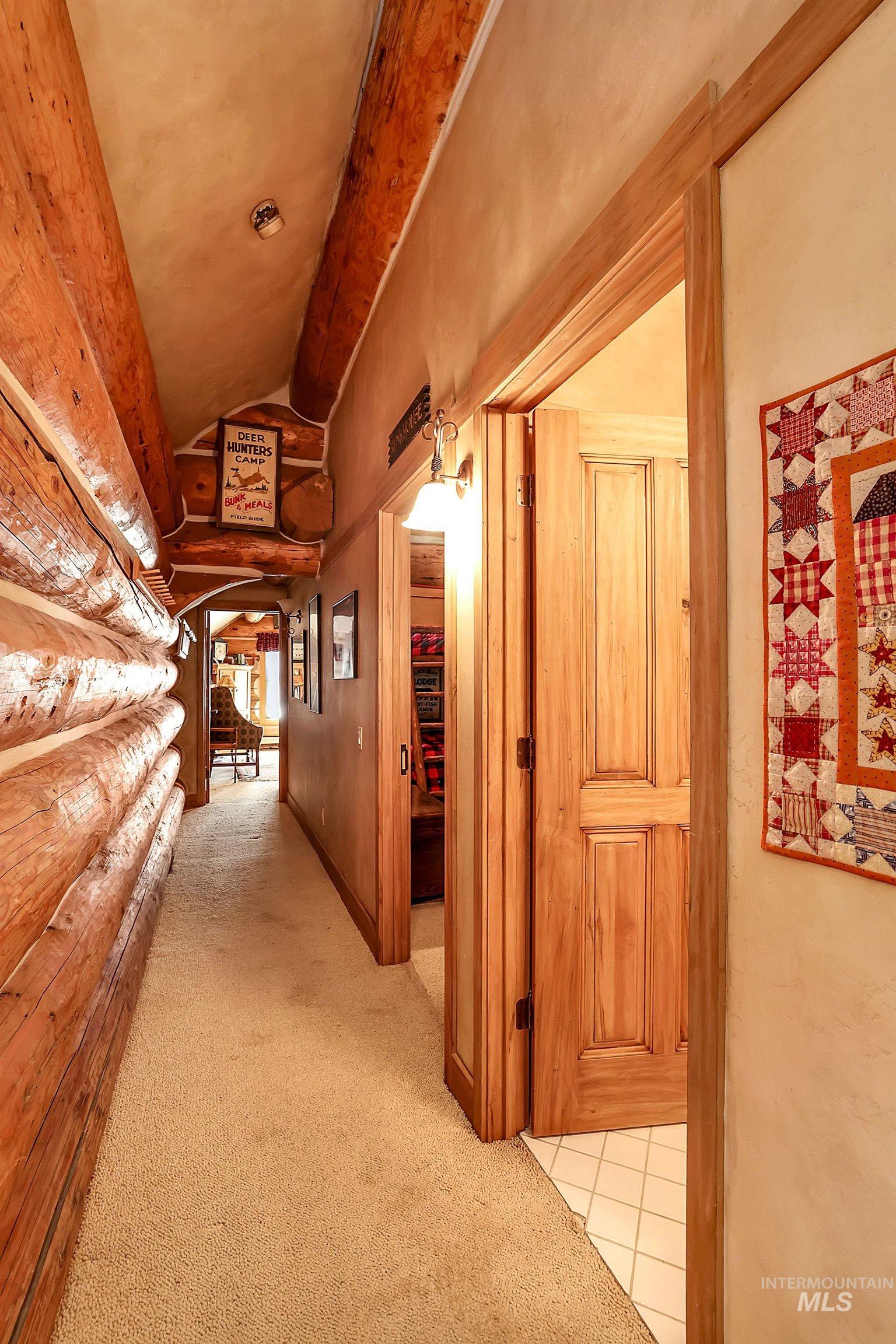 Hallway featuring natural log walls, wood-paneled doors, textured ceilings, and neutral carpet flooring