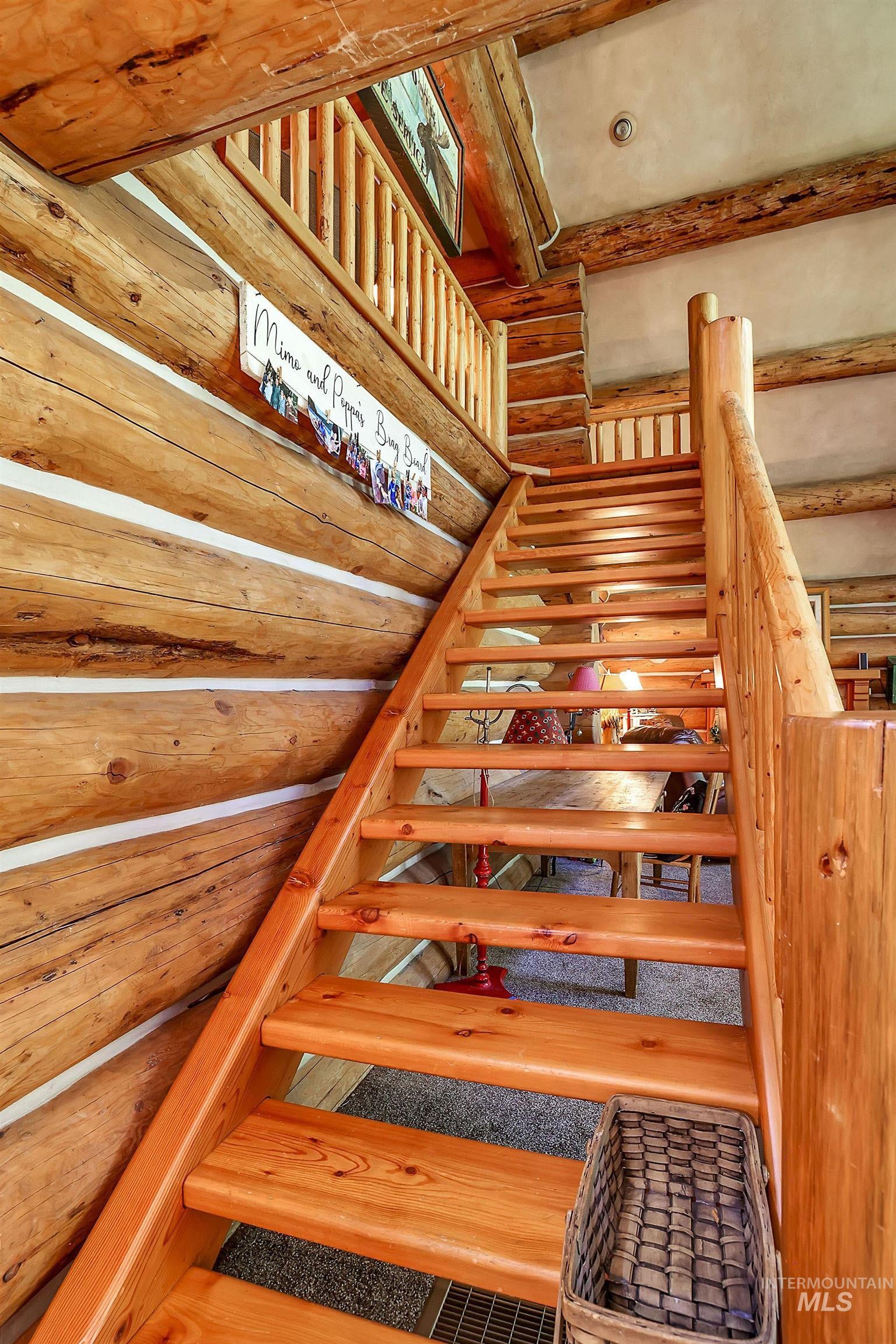 Natural wood staircase with exposed log walls, spindle railing, and exposed ceiling beams