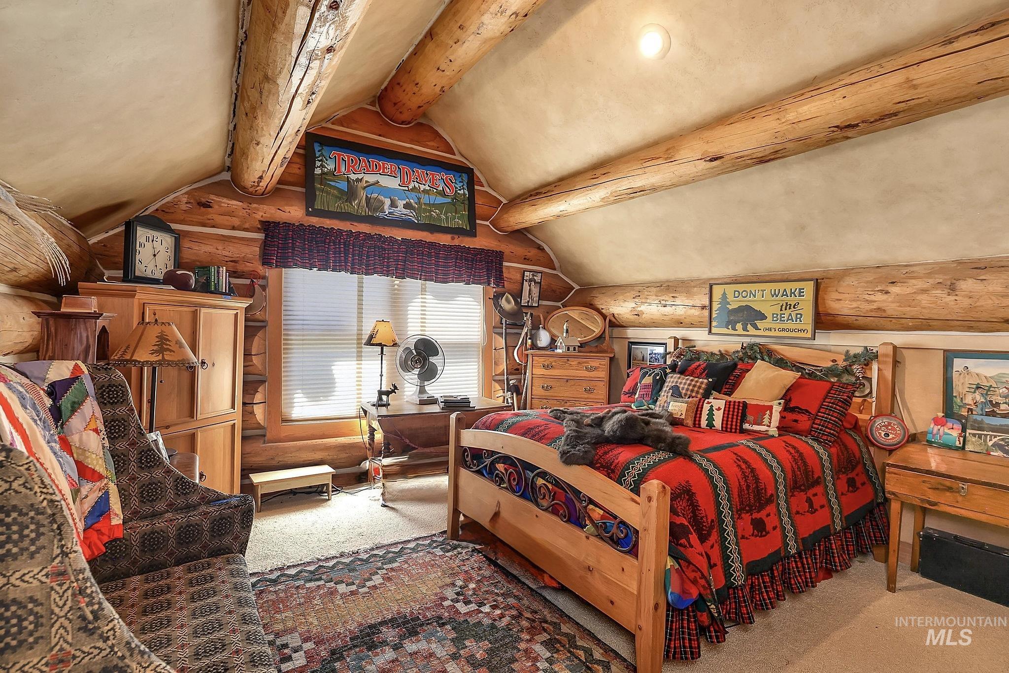 Log-paneled room featuring exposed log beams, a vaulted ceiling, and a prominent window with horizontal blinds