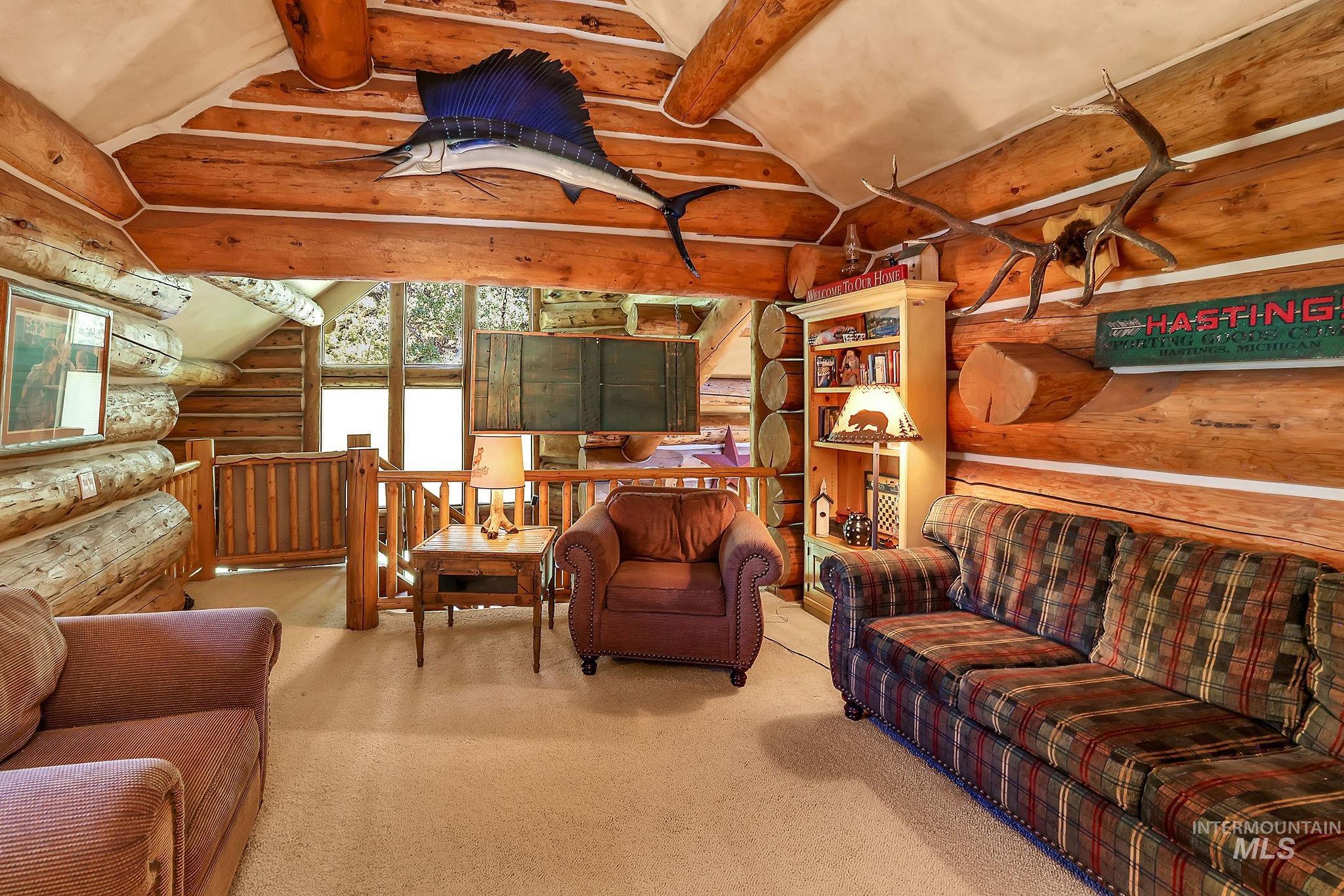 Vaulted ceiling with exposed wood beams, log wall construction, natural wood railing, built-in shelving, and light beige carpeting