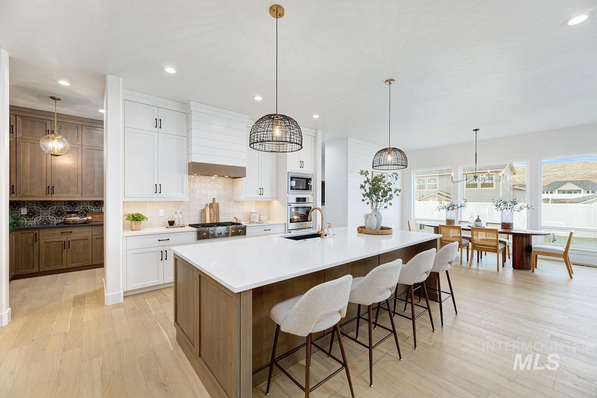 Kitchen featuring pendant lighting, backsplash, a kitchen bar, brown cabinetry, and light wood finished floors
