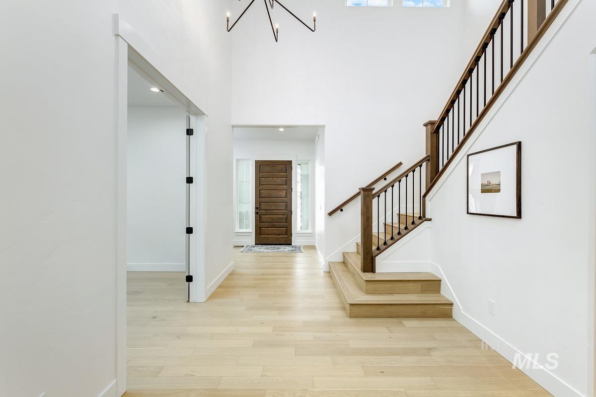 Entryway with light wood-type flooring, a chandelier, stairs, a towering ceiling, and healthy amount of natural light