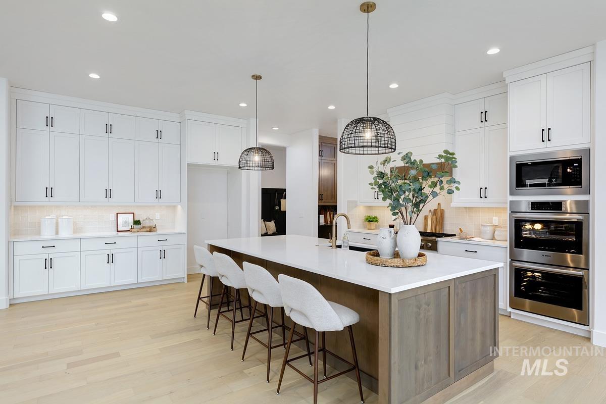 Kitchen featuring tasteful backsplash, light wood finished floors, white cabinetry, a kitchen island with sink, and recessed lighting