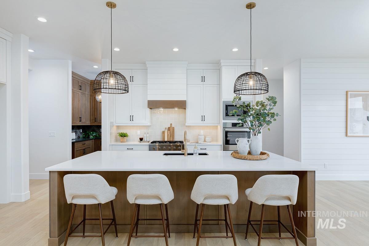 Kitchen featuring tasteful backsplash, light wood finished floors, hanging light fixtures, white cabinetry, and a breakfast bar