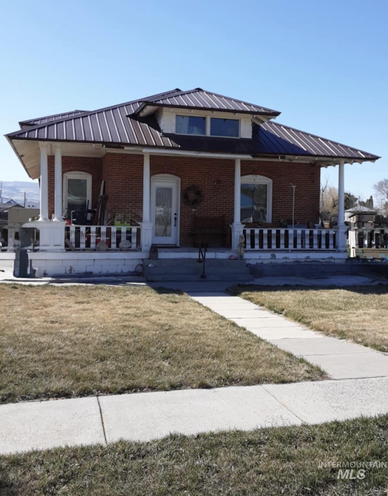 View of front of home featuring a front lawn, brick siding, covered porch, and a standing seam roof