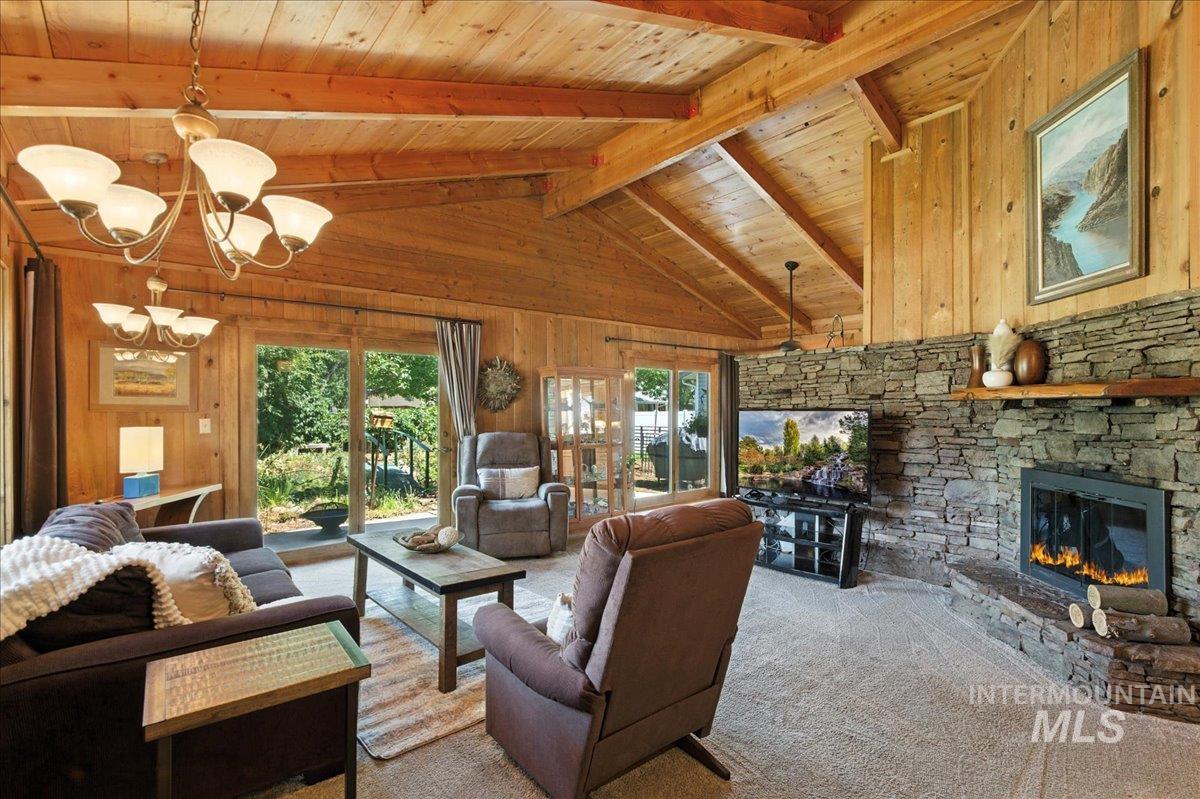 Living room featuring wooden walls, carpet floors, a fireplace, a wood ceiling with exposed beams, and a chandelier