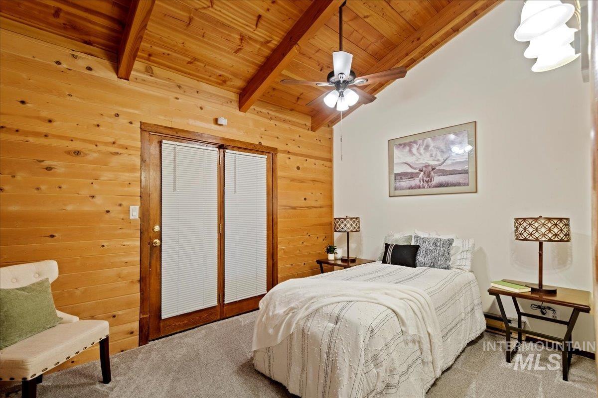 Carpeted bedroom featuring wooden ceiling, wood walls, and a ceiling fan