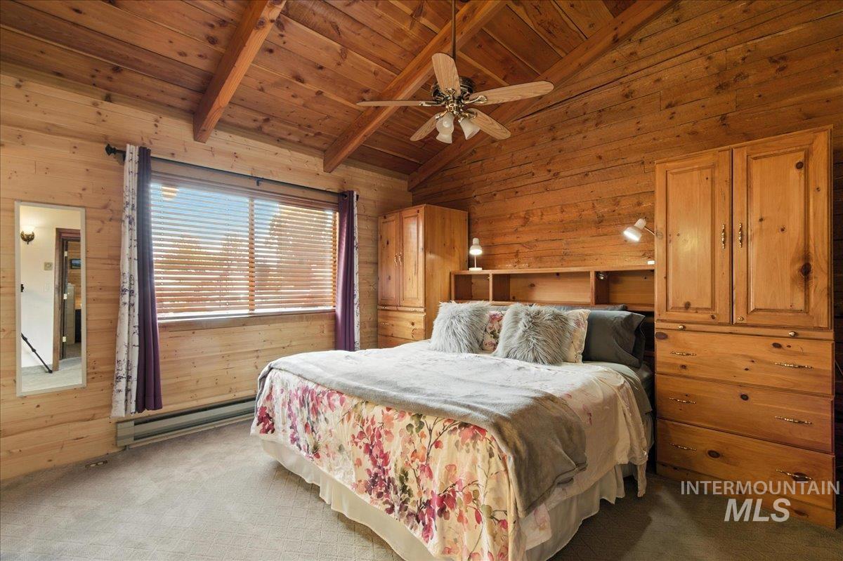 Bedroom featuring wooden walls, carpet floors, a baseboard heating unit, wooden ceiling, and a ceiling fan