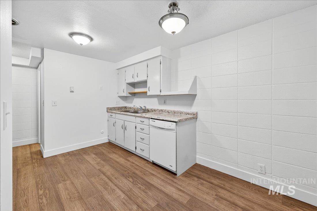 Kitchen with light countertops, dark wood-style floors, white dishwasher, white cabinetry, and a textured ceiling