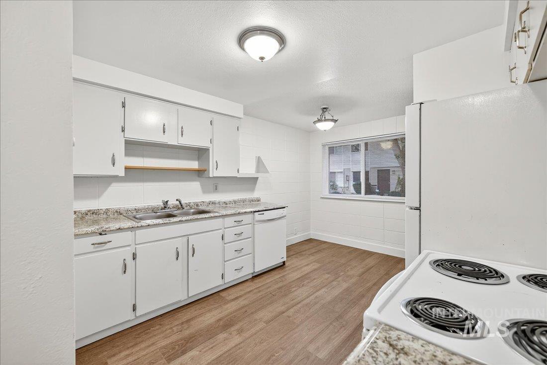 Kitchen featuring light countertops, light wood finished floors, white appliances, white cabinets, and a textured ceiling