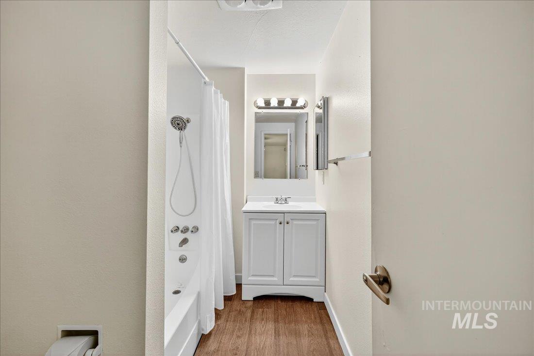 Bathroom with shower / bath combination with curtain, wood finished floors, and vanity