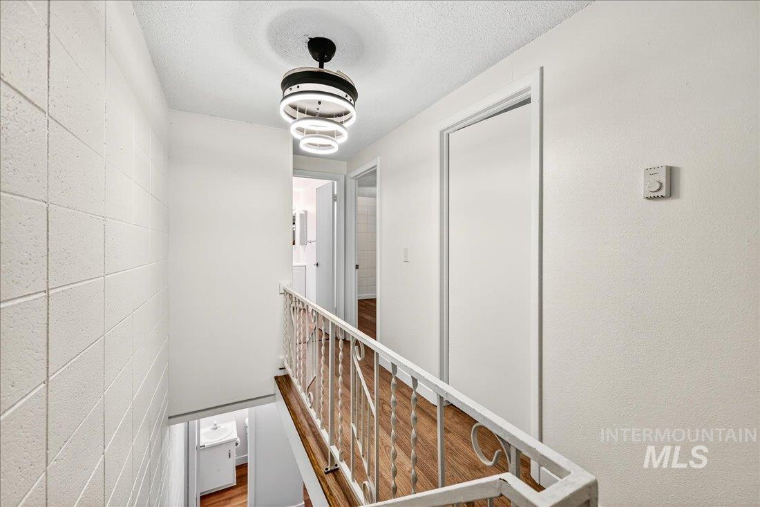 Hallway with concrete block wall, a textured ceiling, an upstairs landing, and wood finished floors
